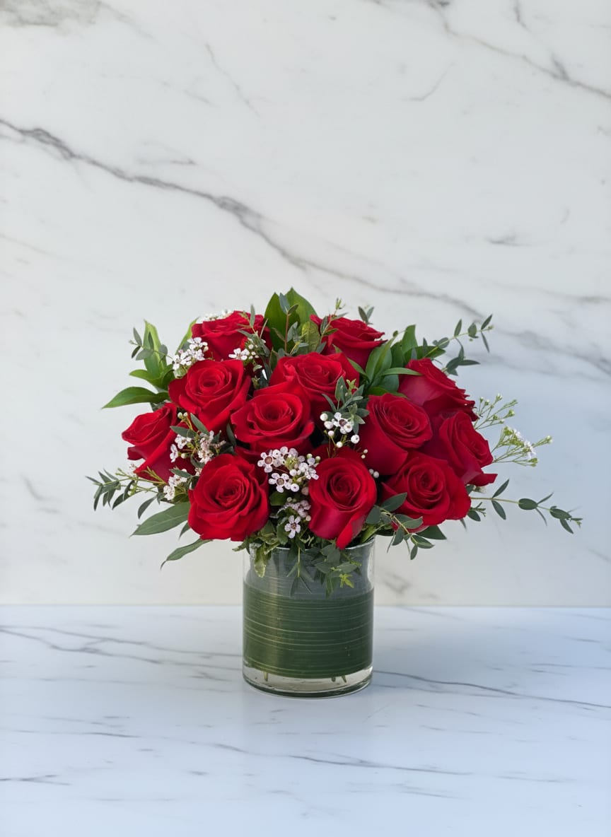 Romance &amp; Red Roses - A timeless expression of love, our Romance and Red Roses arrangement features lush, velvety red roses surrounded by soft greenery and delicate accent blooms. Handcrafted to capture passion and elegance, this classic bouquet is perfect for anniversaries, romantic gestures, or simply saying “I love you.”    Each stem is artfully arranged in a modern glass vase, creating a striking yet refined display that radiates warmth and sophistication. Available in 12, 18 or 24