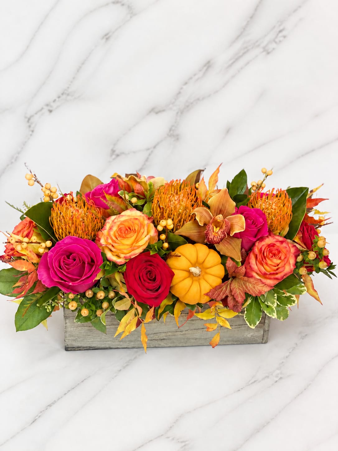 Autumn floral arrangement with roses, orchids, and a small pumpkin in a wooden box