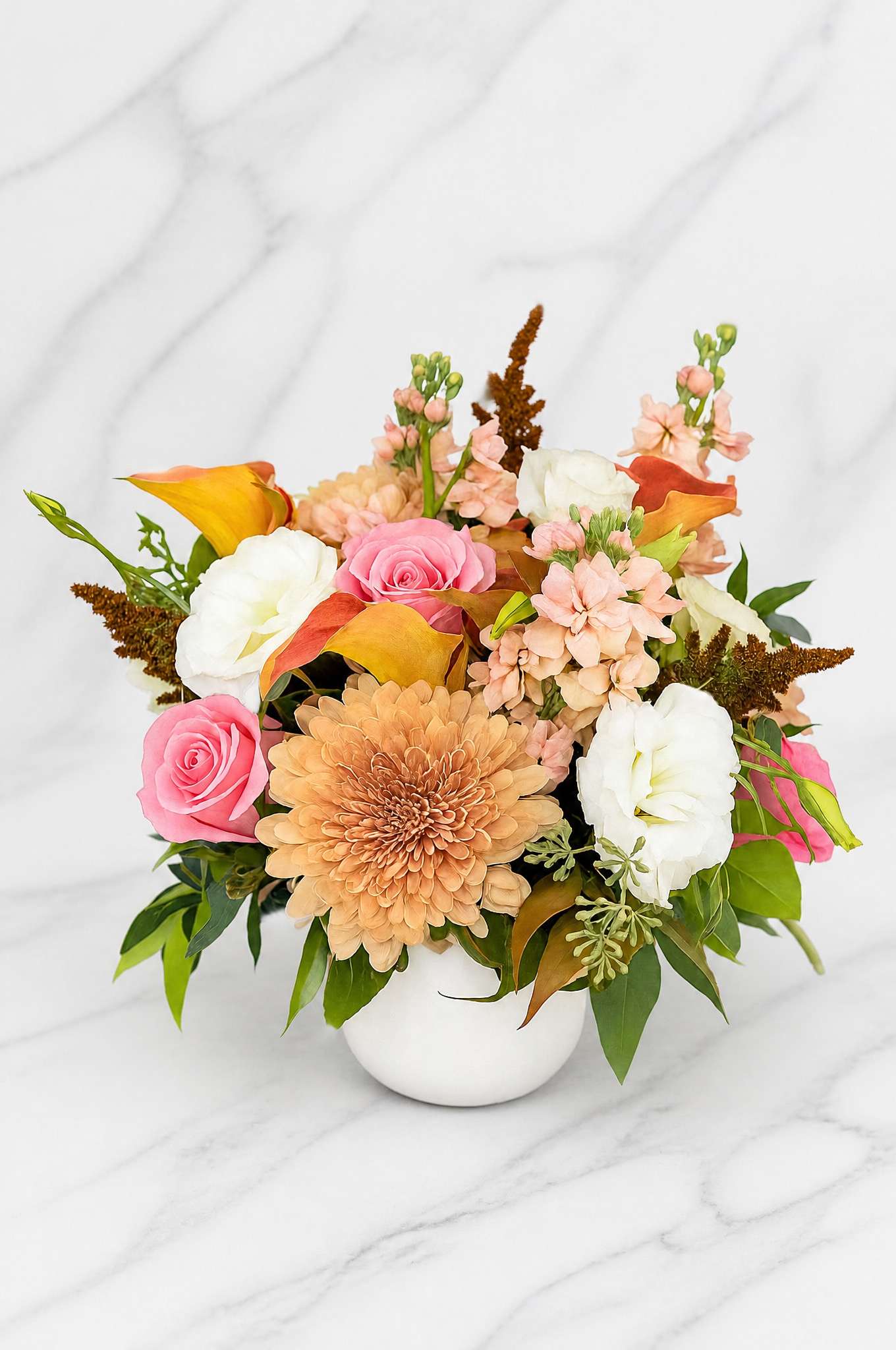 Mixed bouquet in a white vase with pink roses, white blooms, and peach flowers