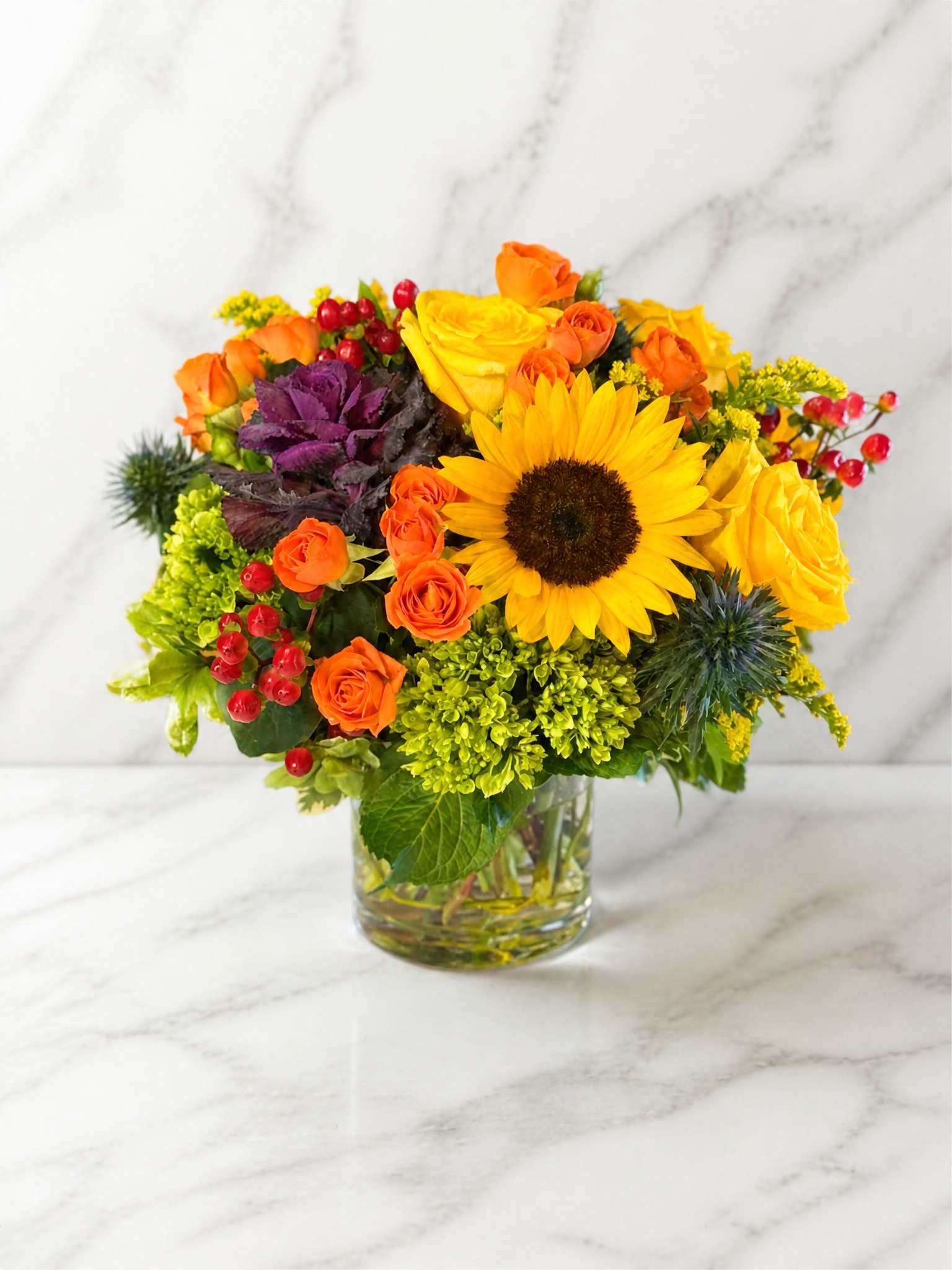 Bright mixed bouquet with sunflowers, orange roses, and red berries in a glass vase