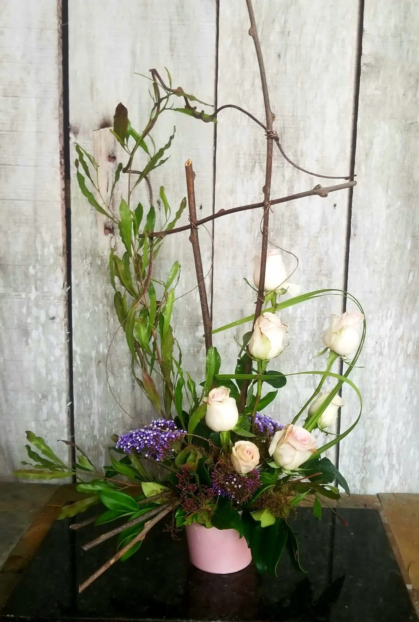 Tall floral arrangement with white roses and purple accents in a pink vase