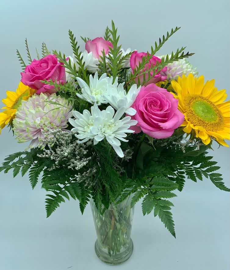 Bouquet of pink roses, white daisies, and yellow sunflowers in a glass vase