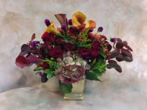 Mixed bouquet with calla lilies and dark purple flowers in a square vase