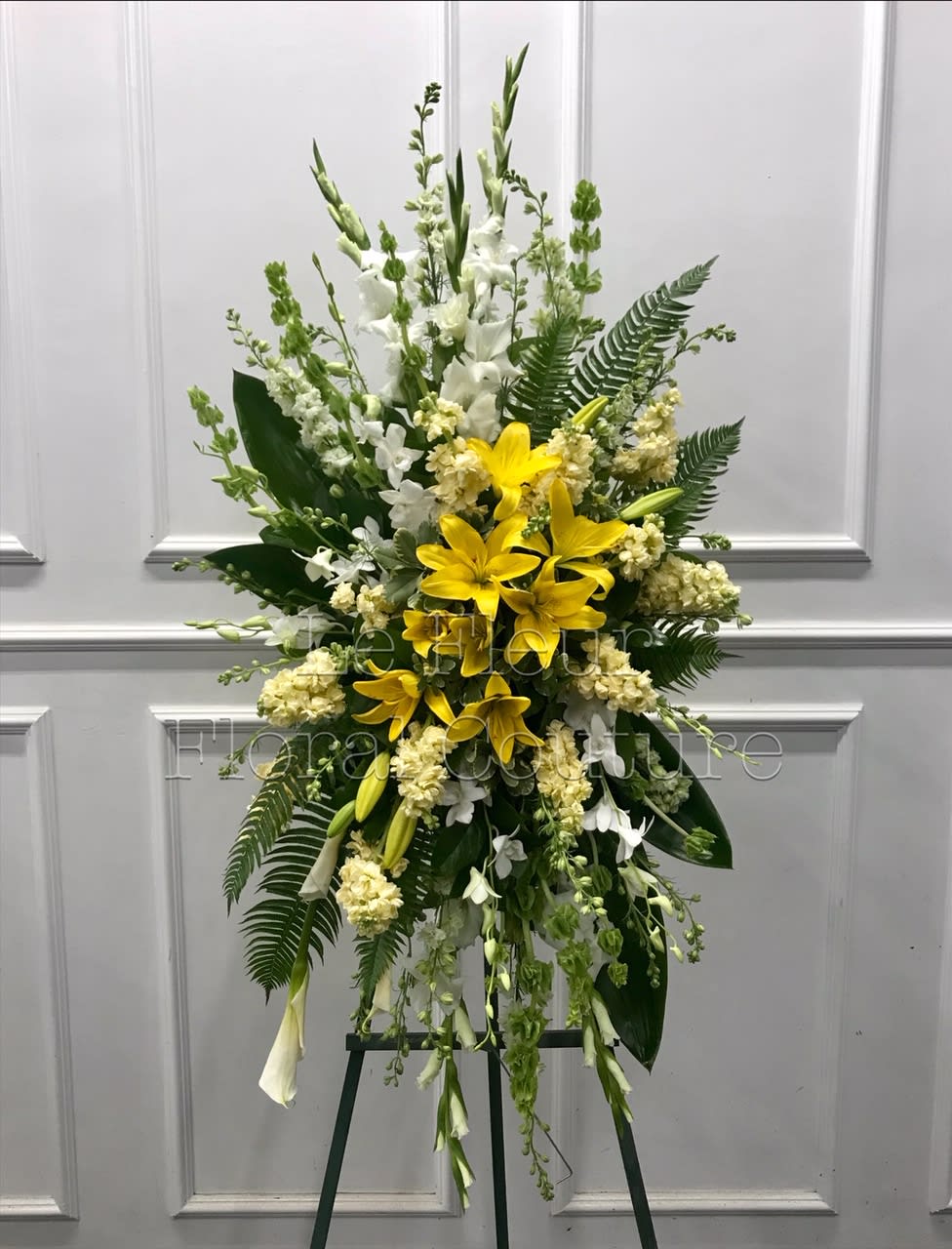 Standing floral spray with yellow lilies and white flowers on an easel