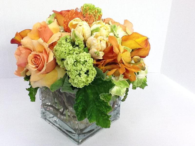 Orange and peach roses with green blooms in a square glass vase