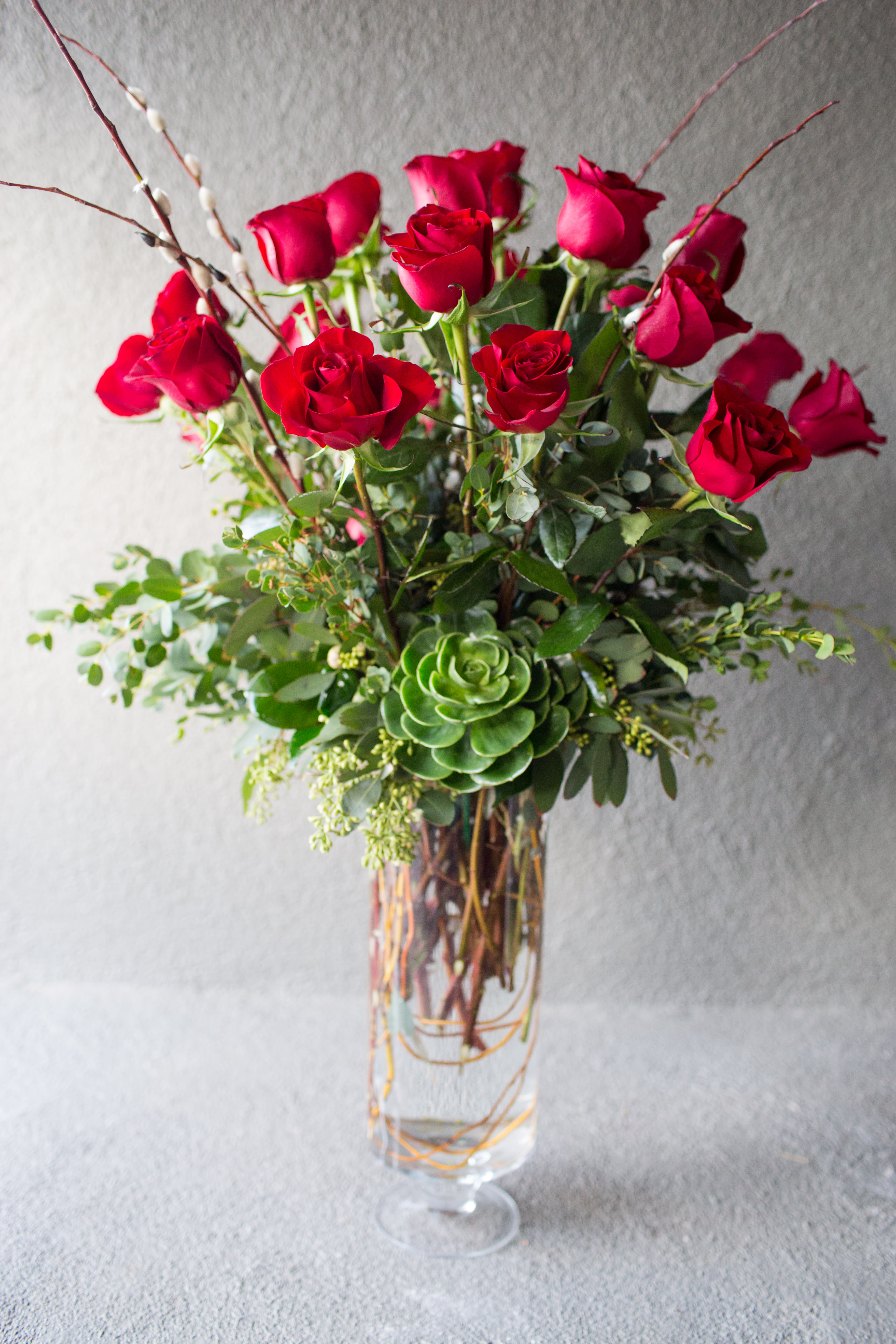 Red roses arranged in a clear glass vase with greenery and a succulent accent