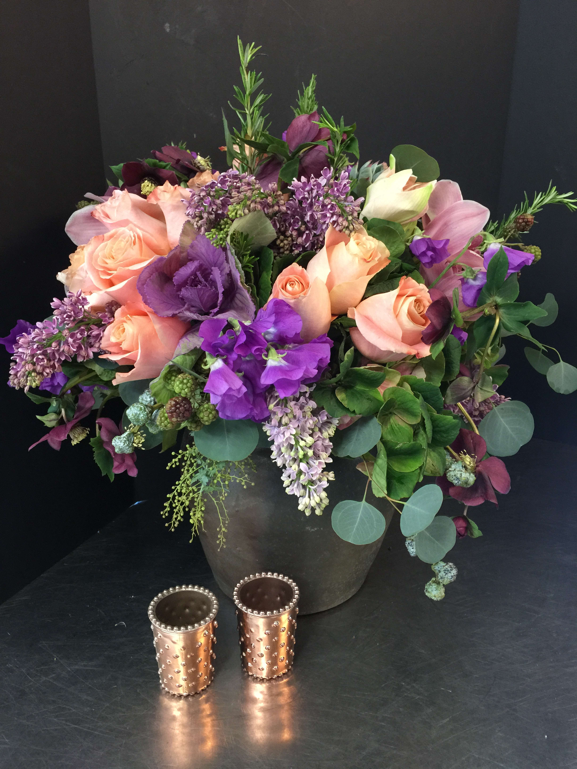 Mixed bouquet of peach roses and purple flowers in a dark vase