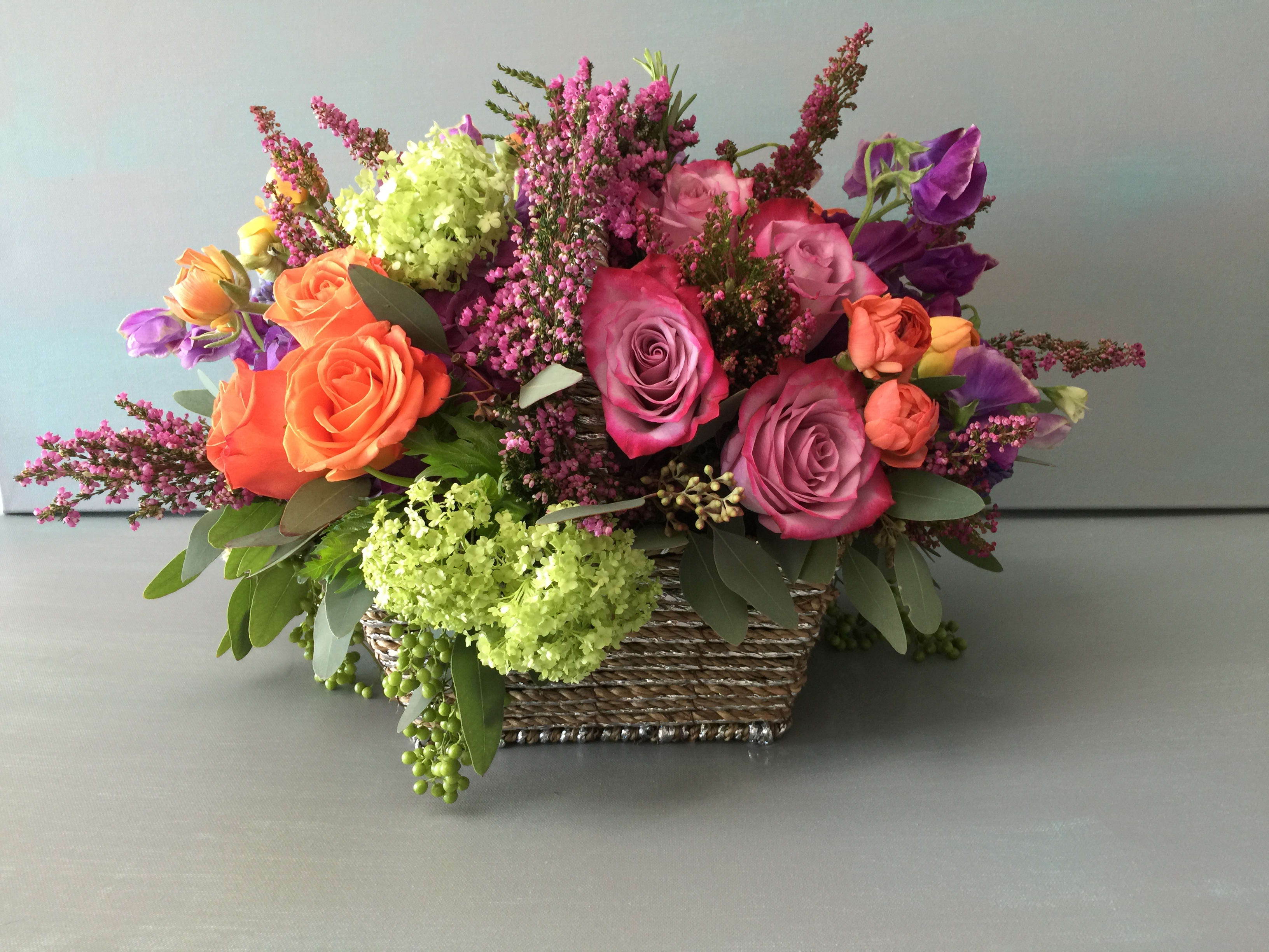 Mixed bouquet of roses and purple flowers in a woven basket