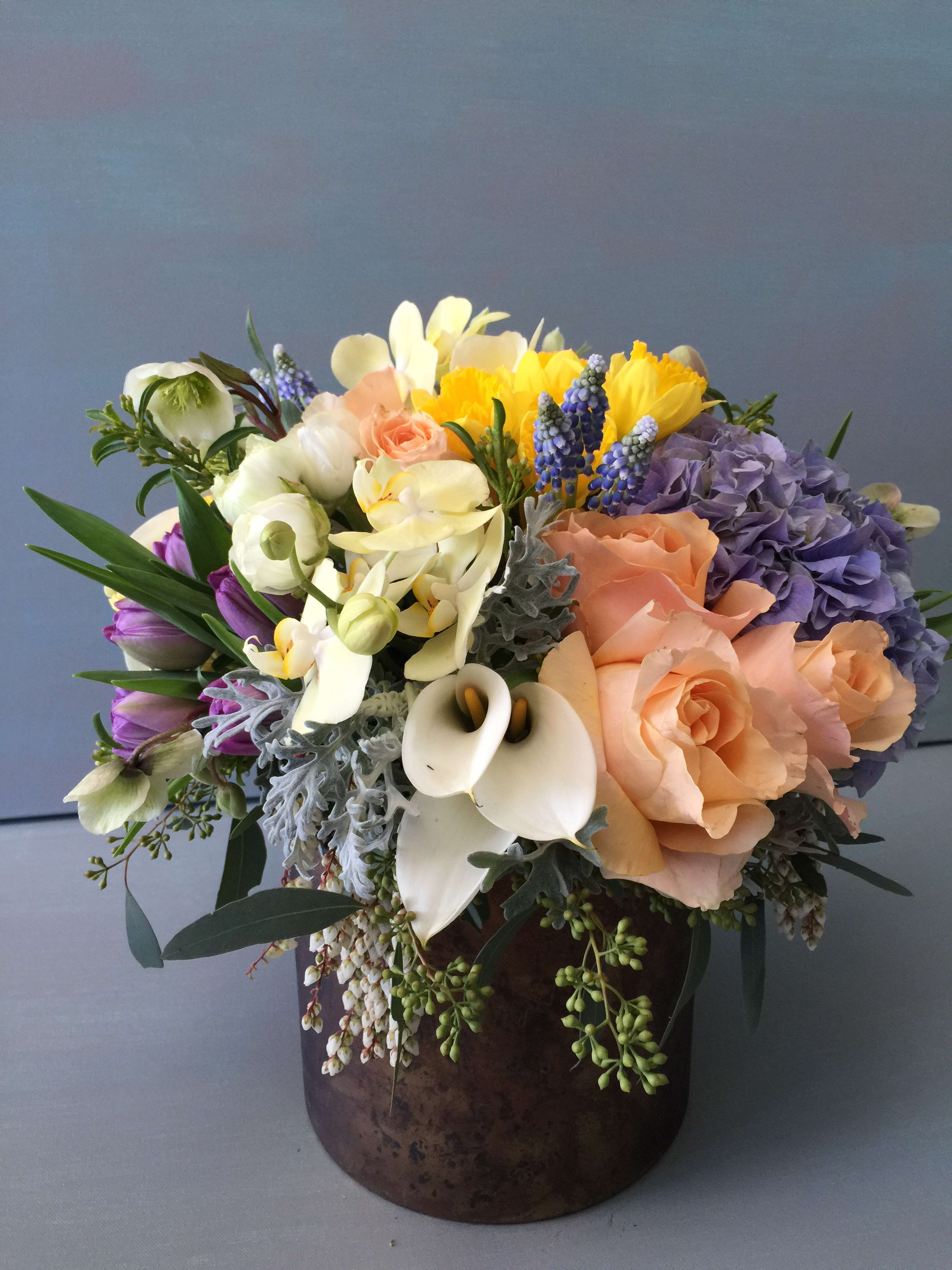 Mixed bouquet of peach, purple, white, and yellow flowers in a dark vase