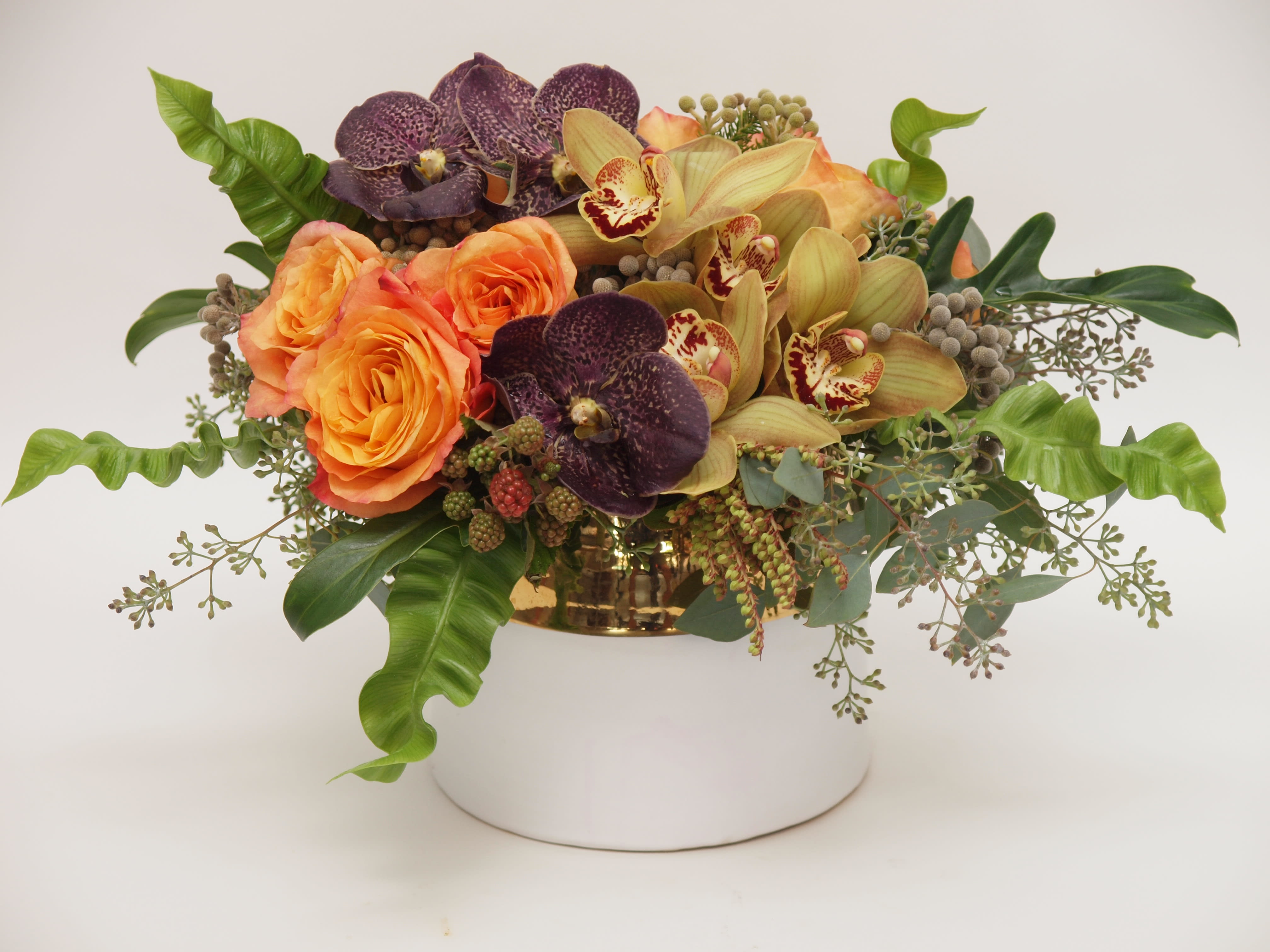Orange roses and orchids arranged in a gold container