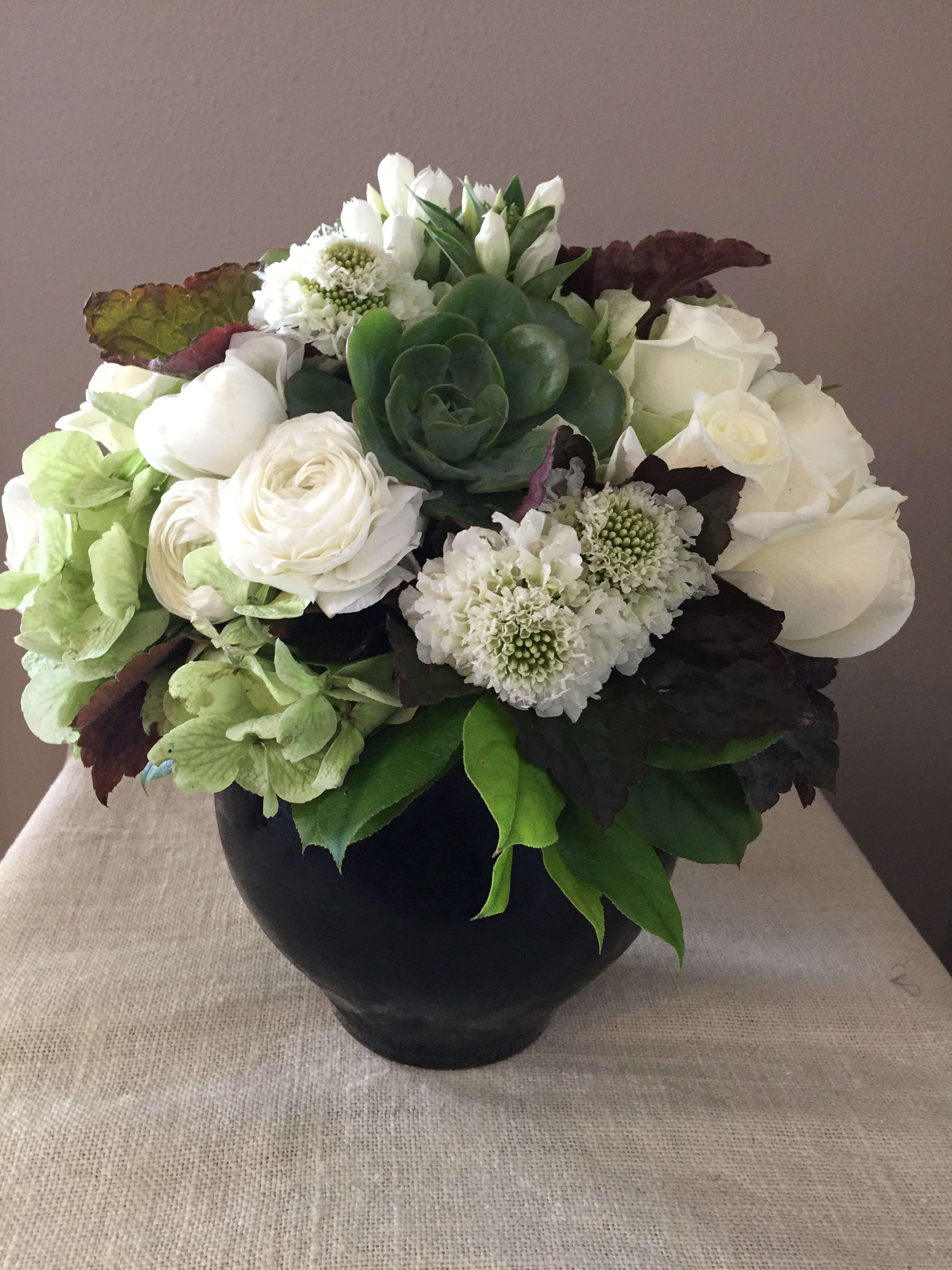 White floral arrangement in a black vase with a green succulent center