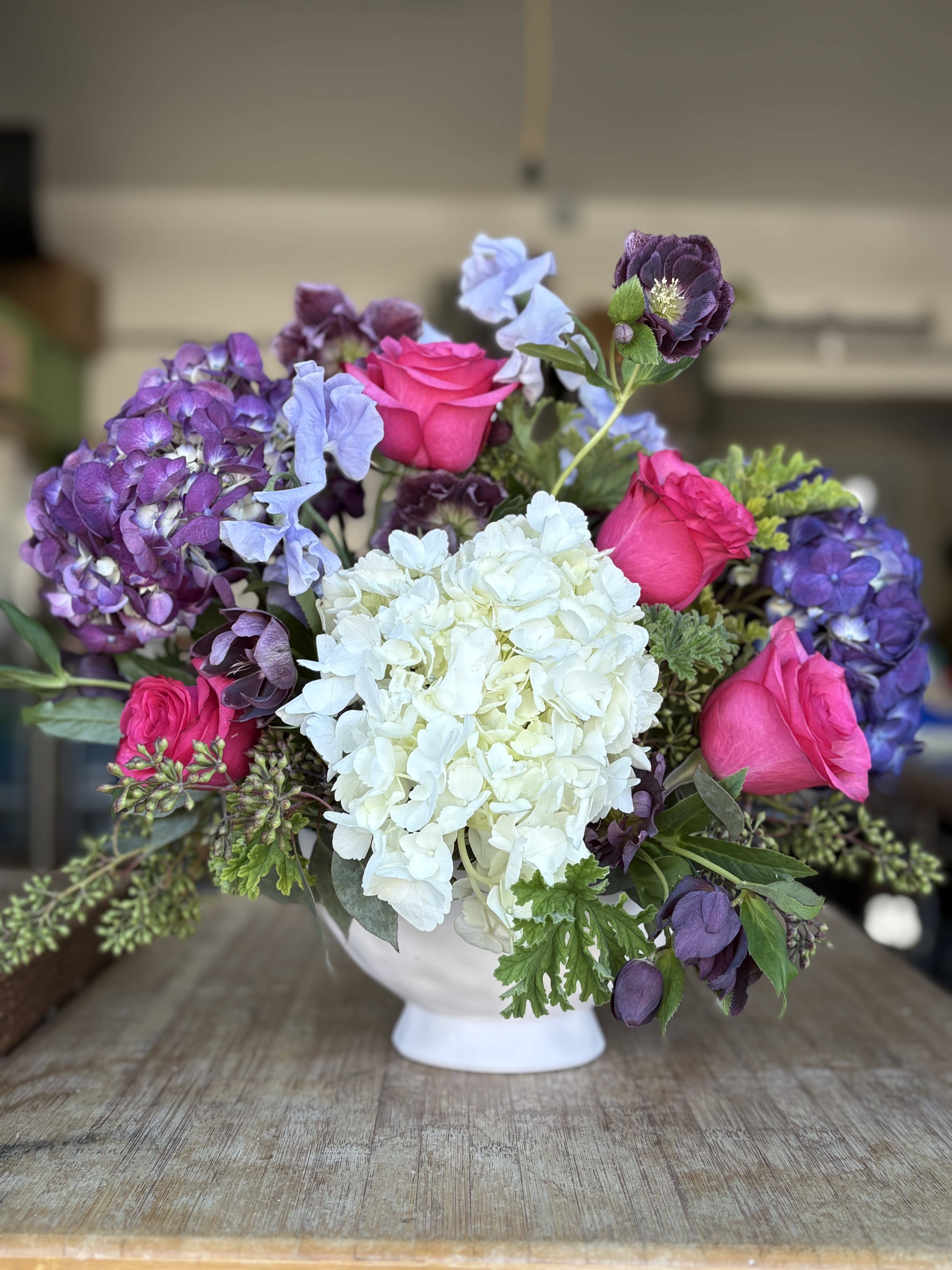 Bouquet of pink roses, white hydrangea, and purple blooms in a white vase