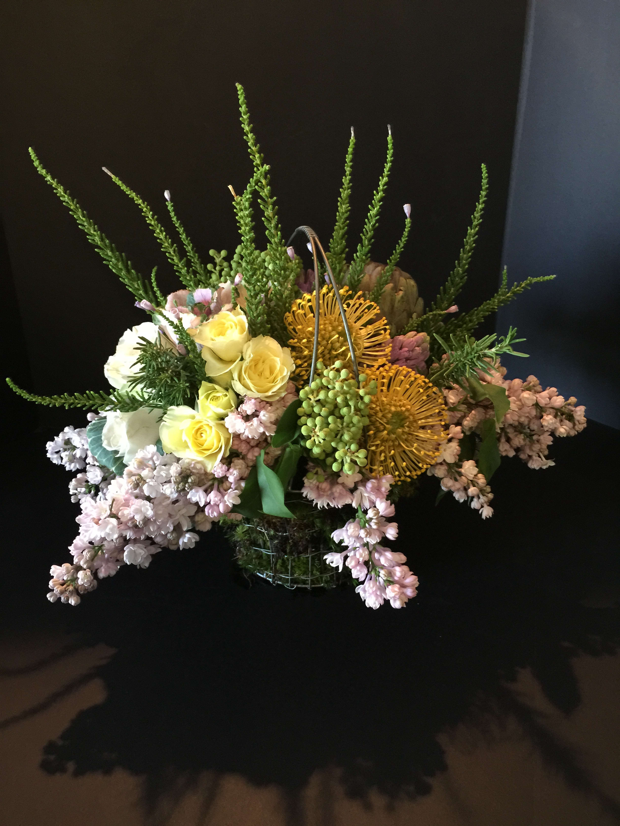 Mixed floral arrangement with yellow roses and pink blooms in a wire basket