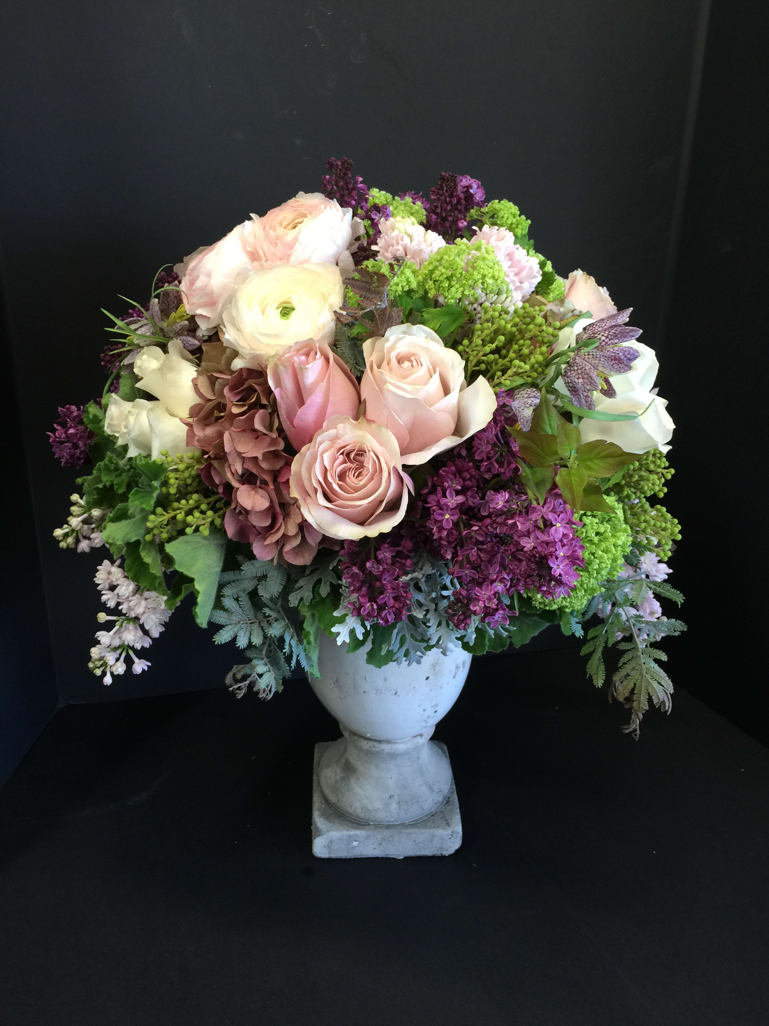 Pastel bouquet of roses, ranunculus, and purple blooms in a white urn vase