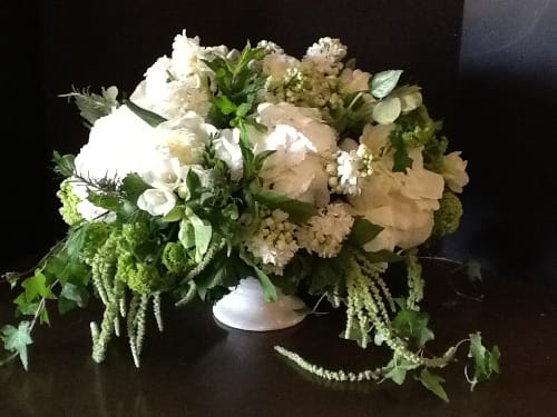 White floral arrangement in a low white vase with trailing greenery