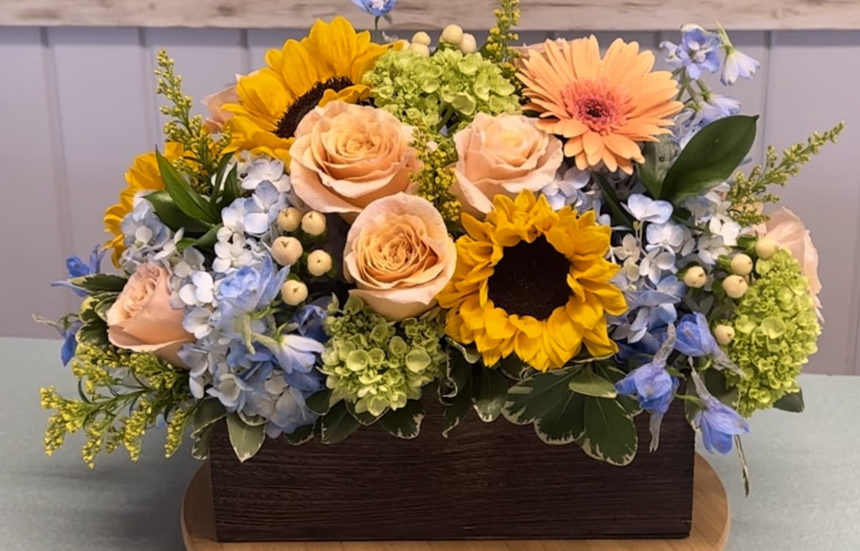 Mixed bouquet with sunflowers, peach roses, and blue hydrangeas in a wooden box