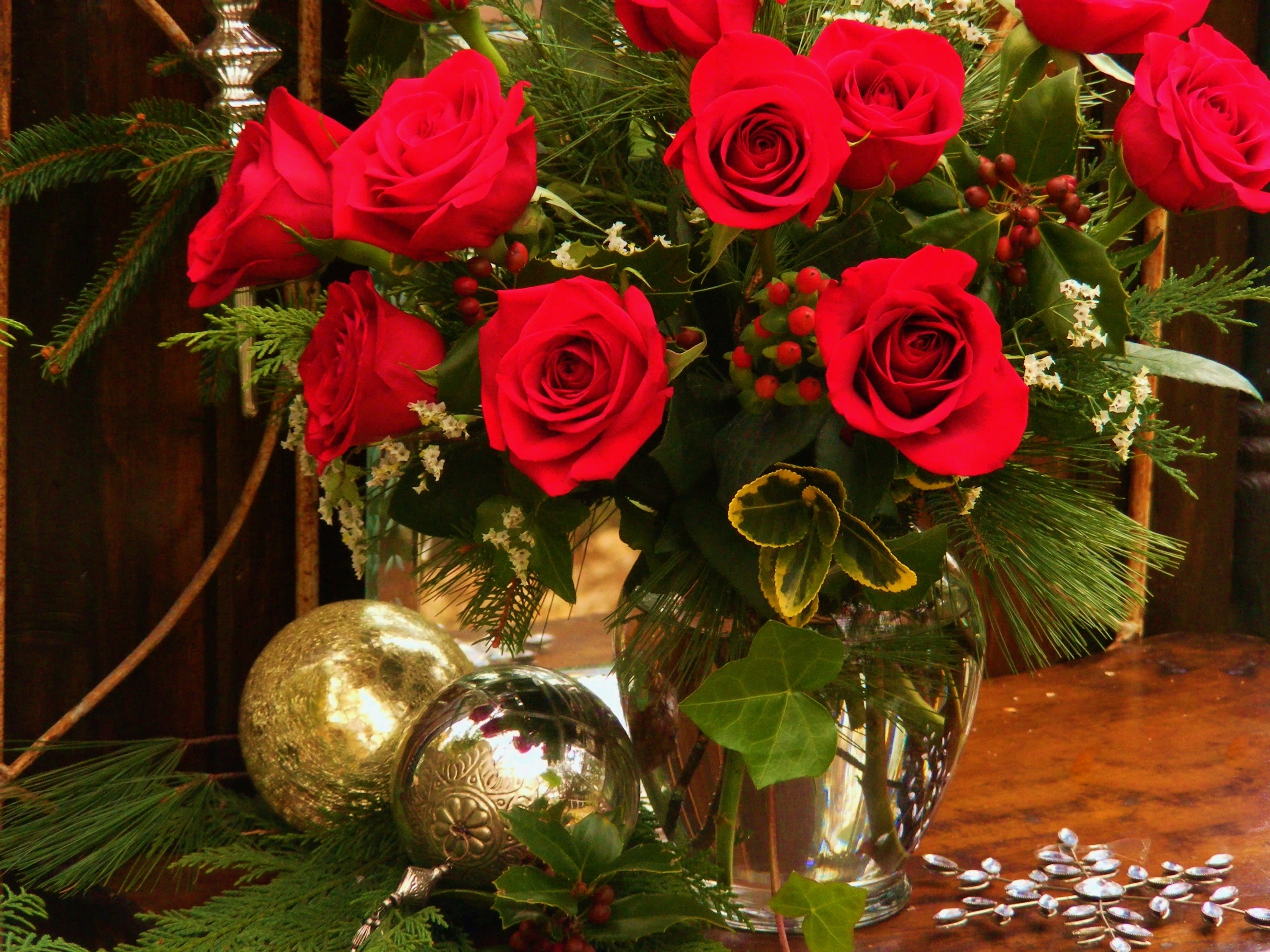 Red roses arranged in a clear glass vase with evergreen accents