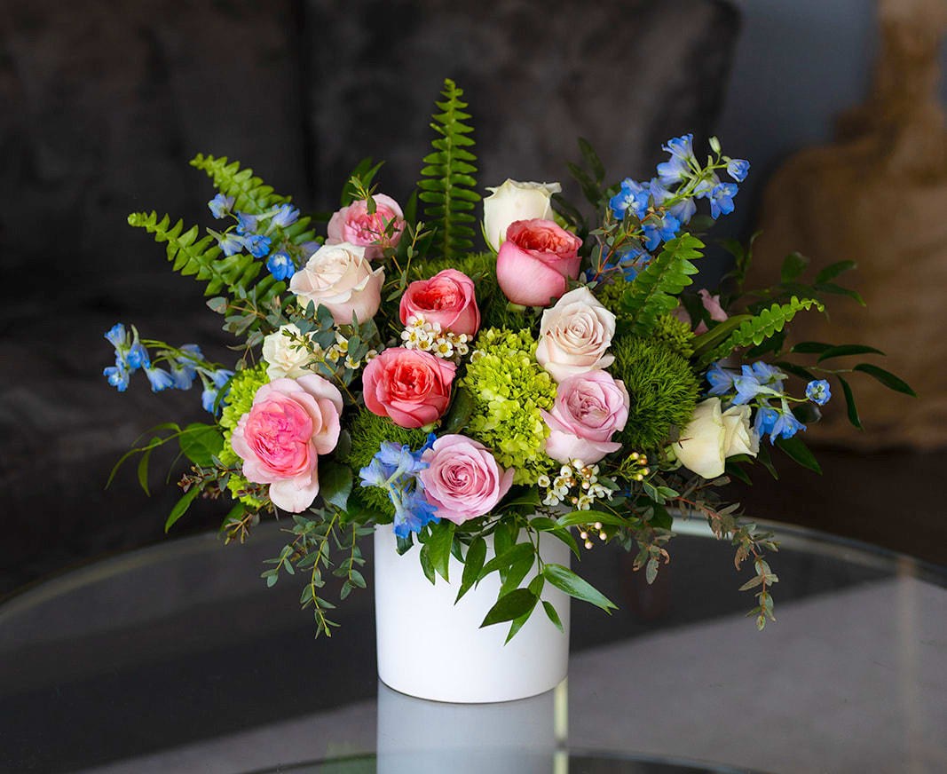 Arrangement of pink and cream roses with blue blooms in a white vase