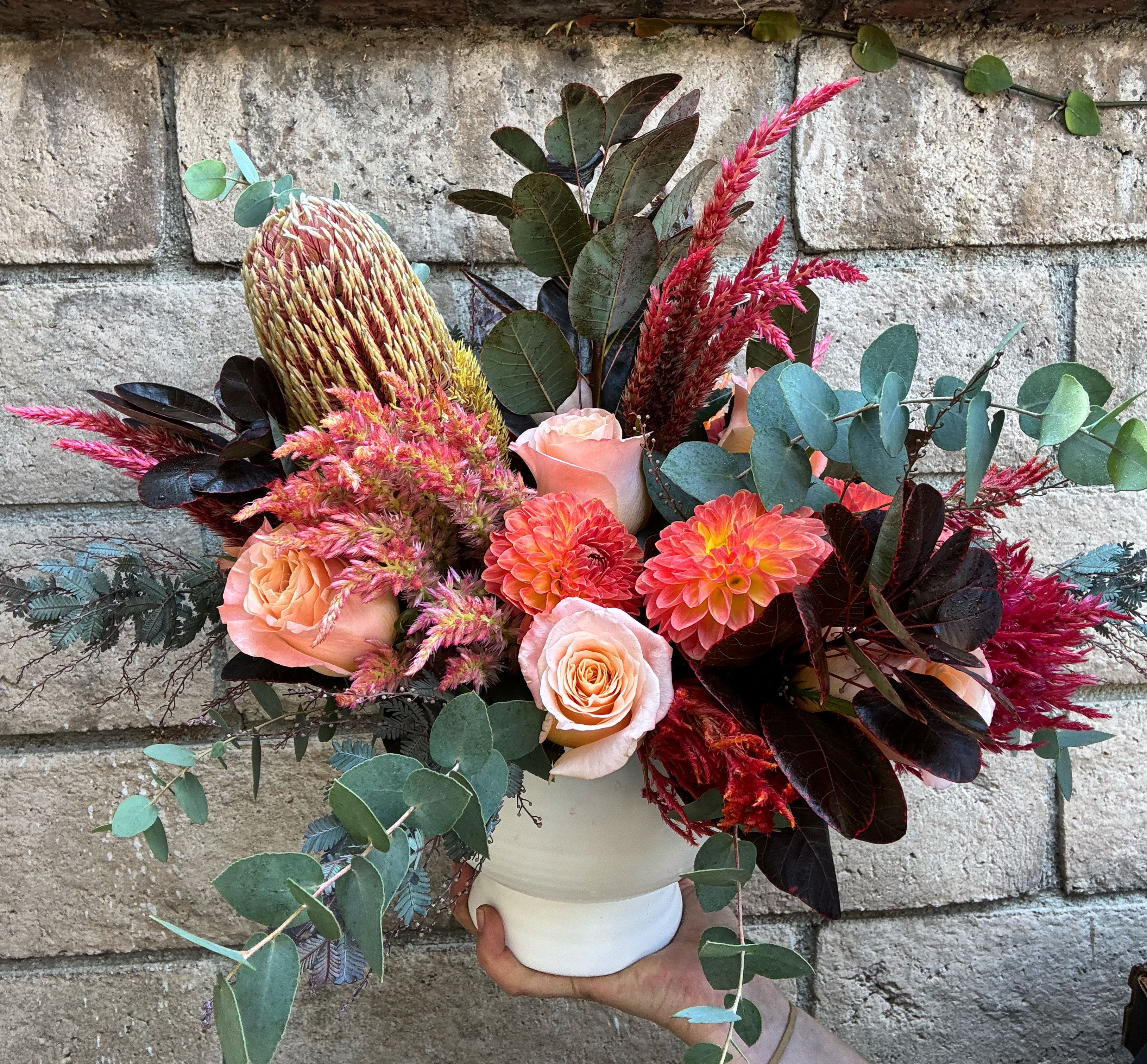 Bouquet of peach roses, coral dahlias, and pink-red blooms in a white vase
