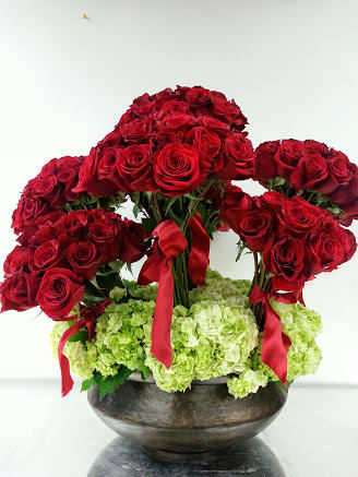 Red rose arrangement with green hydrangeas in a dark bowl vase