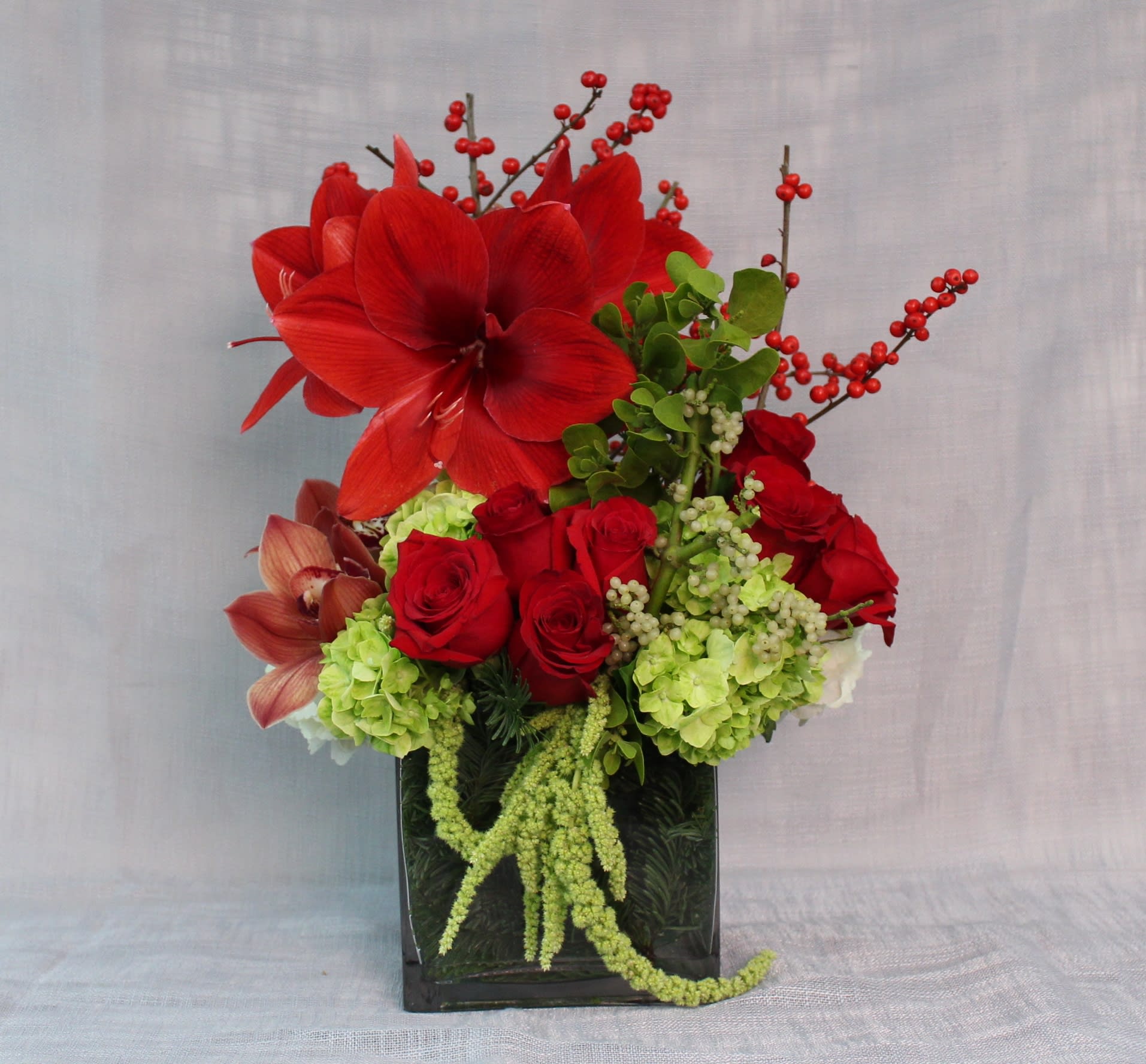 Red amaryllis and roses in a black vase with green hydrangeas