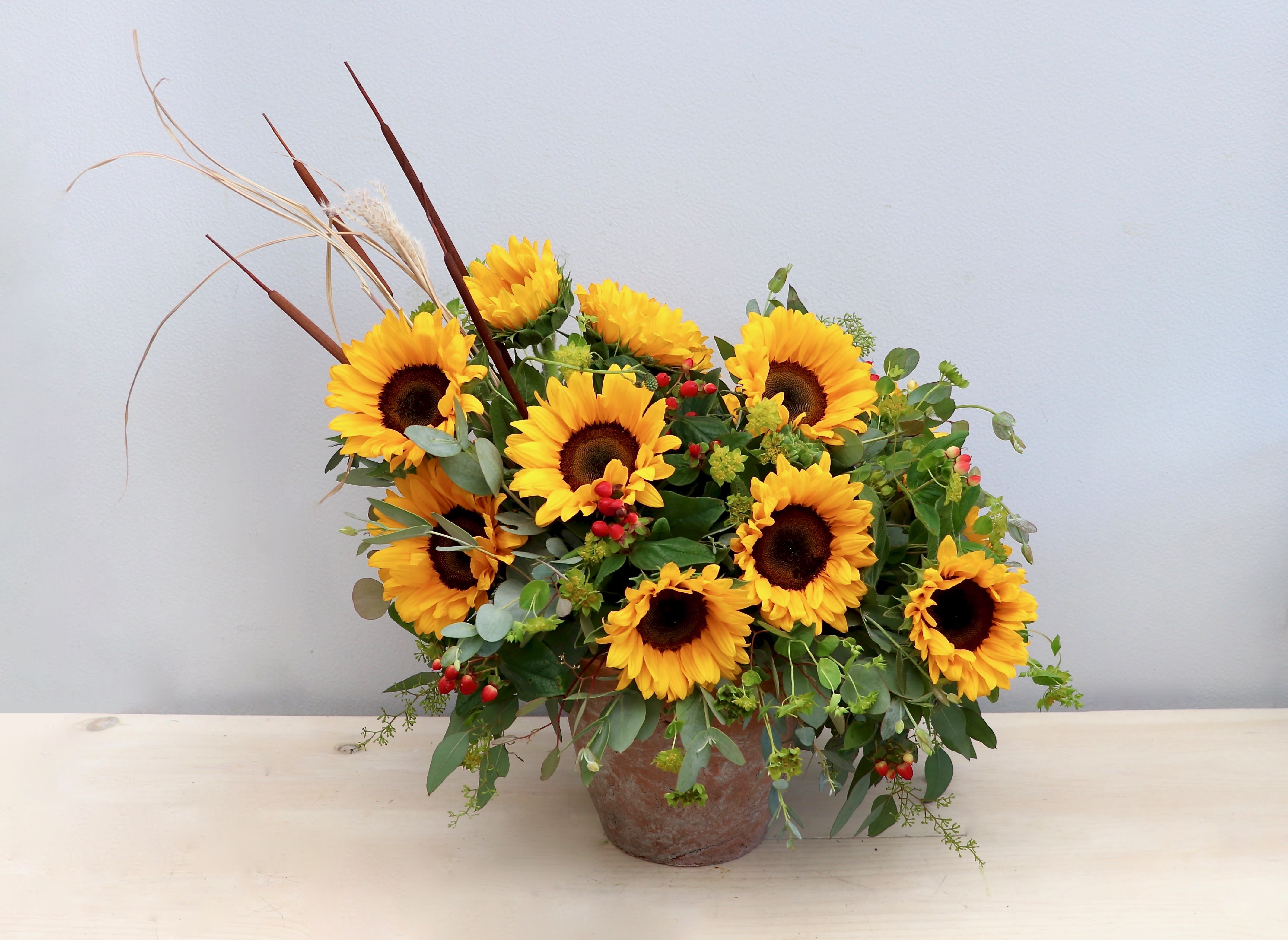 Asymmetrical arrangement of yellow sunflowers with red berries in a rustic pot
