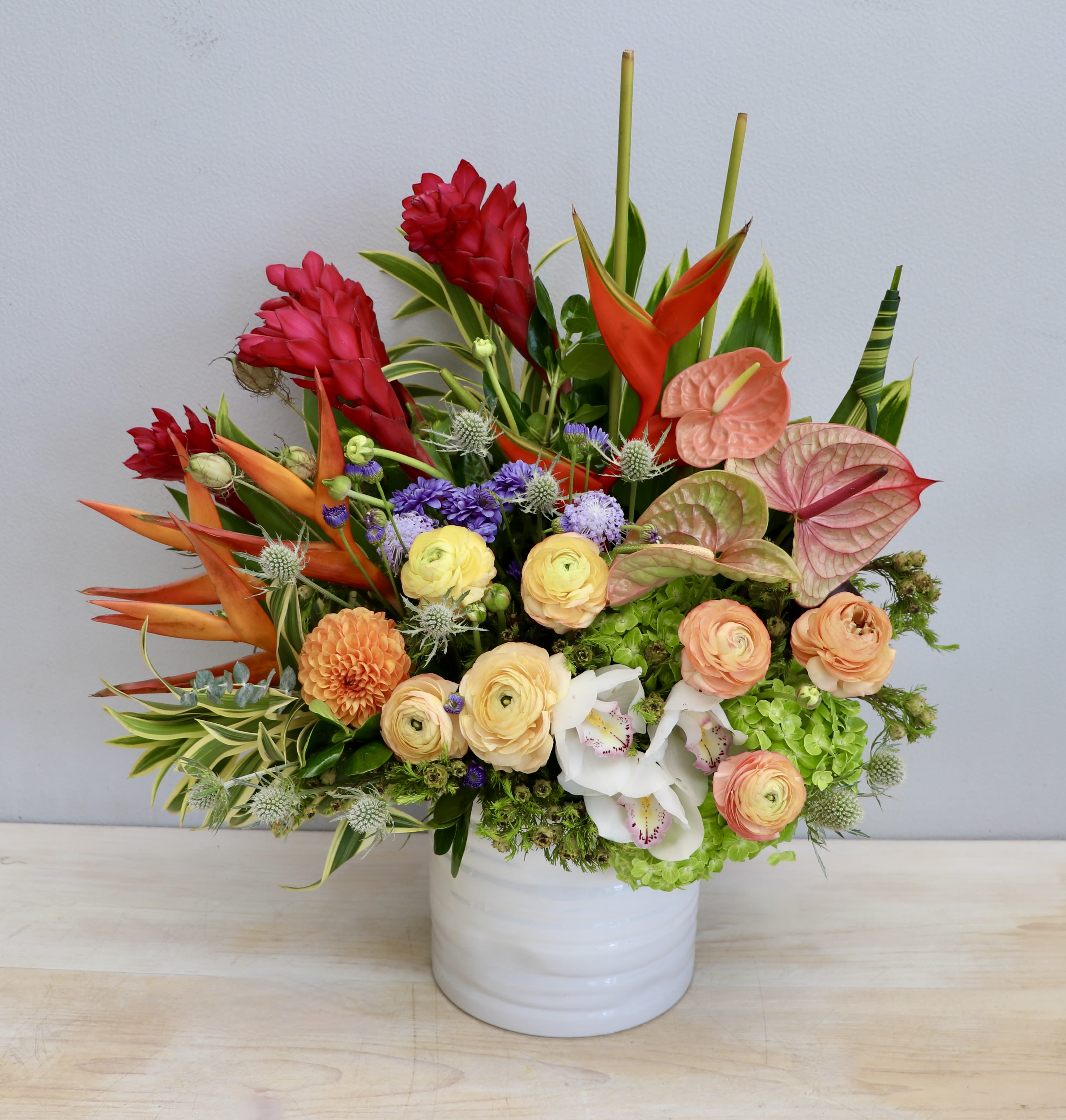 Colorful tropical flower arrangement in a white ceramic cylinder vase