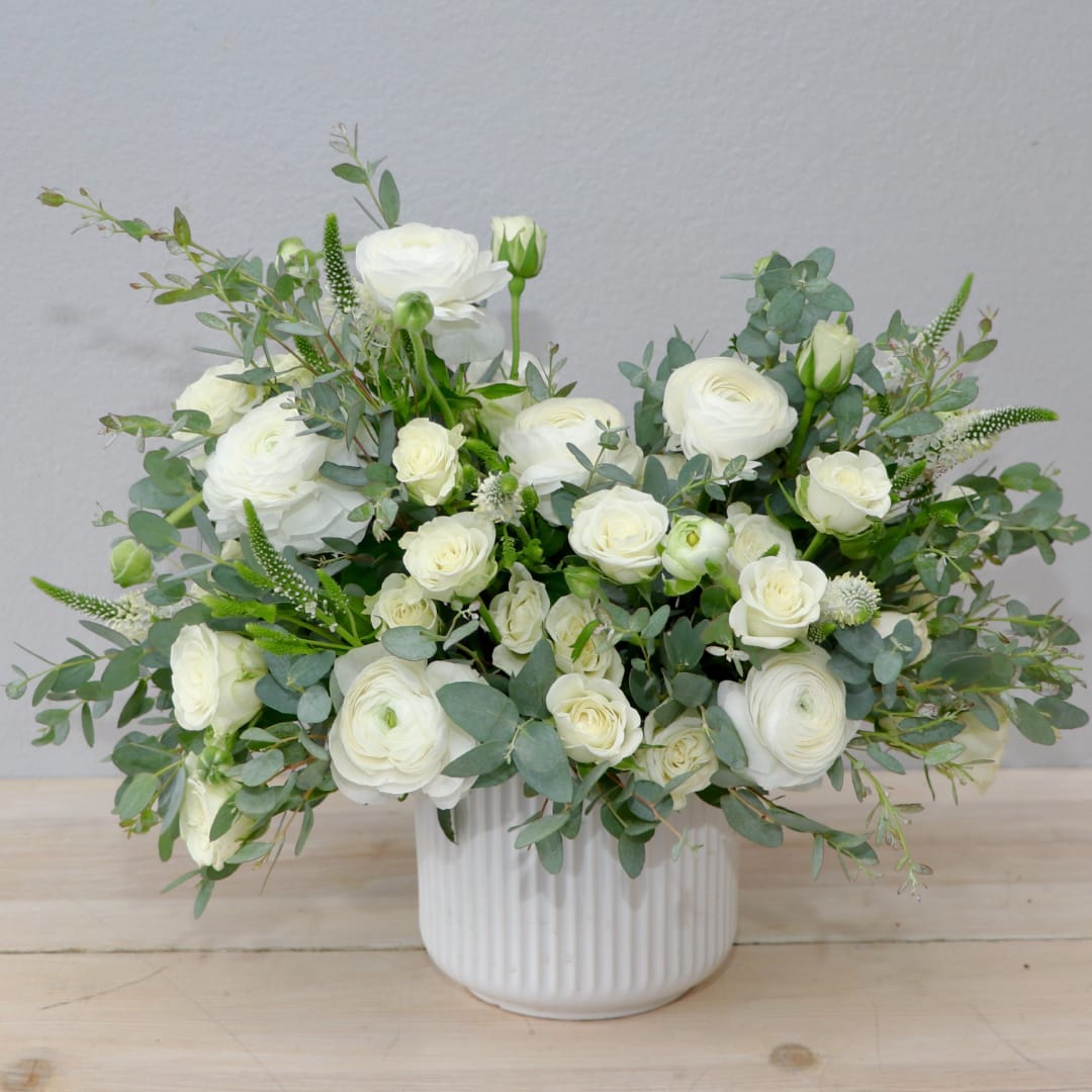White rose and ranunculus arrangement in a ribbed white vase