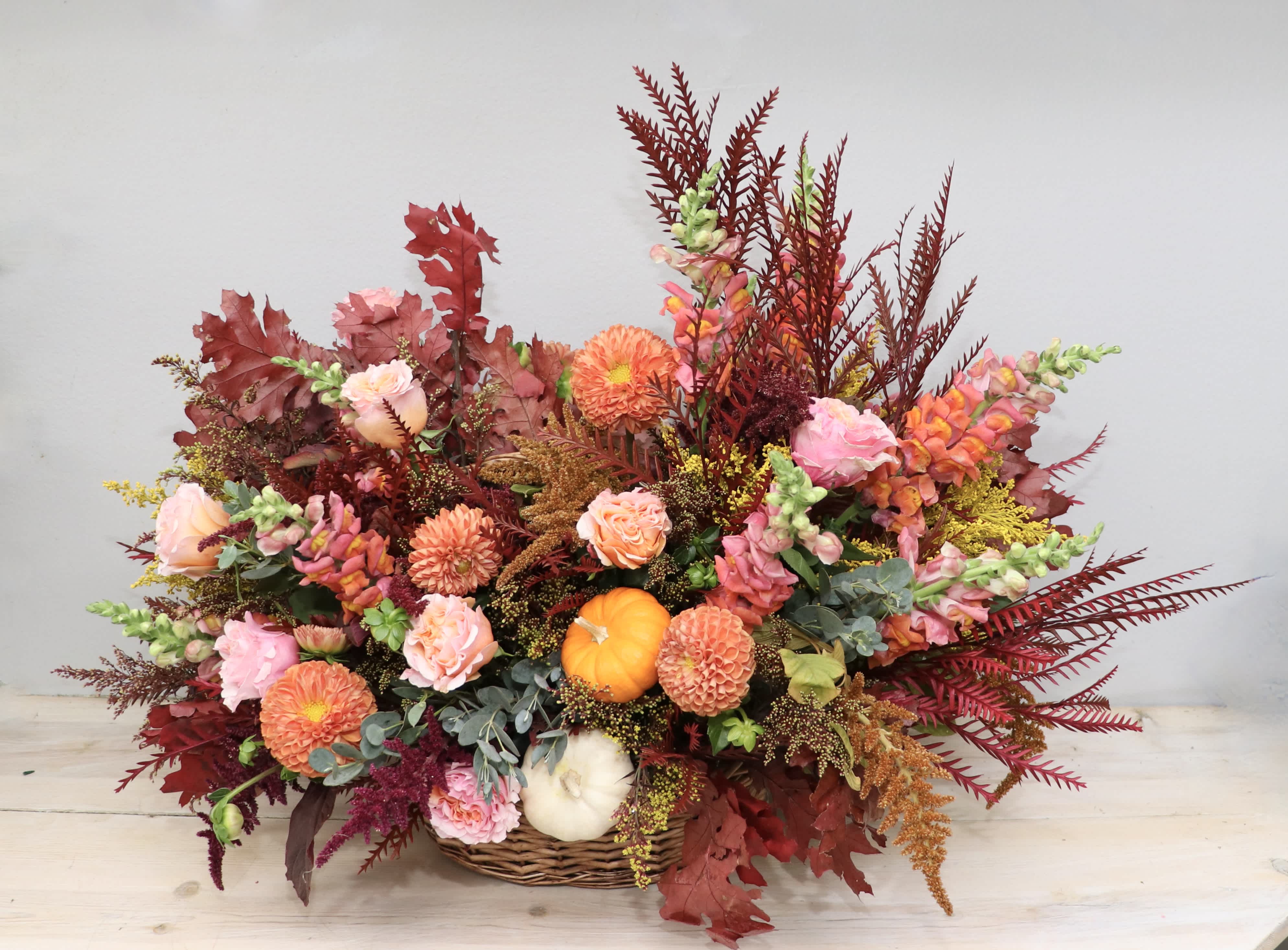 Autumn floral arrangement in a wicker basket with orange and pink blooms