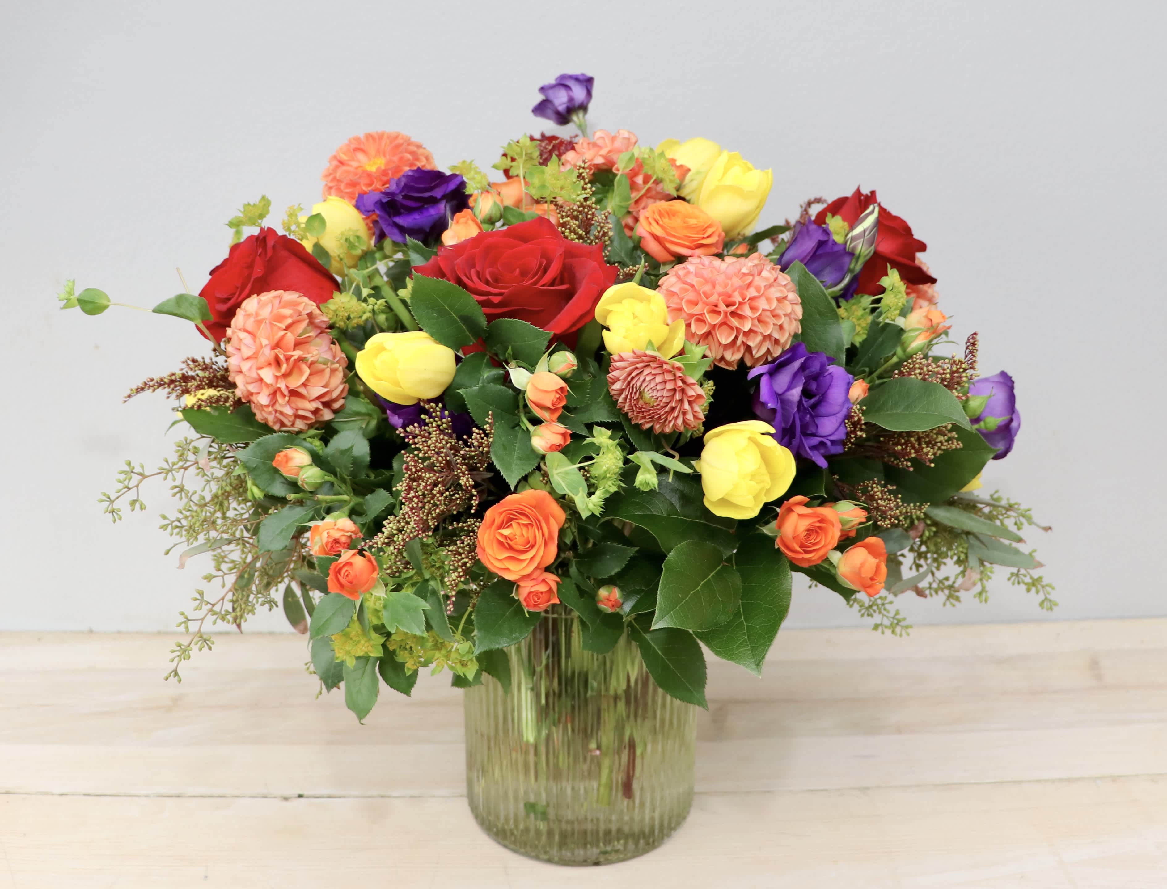 Mixed bouquet of roses, tulips, and dahlias in a glass vase