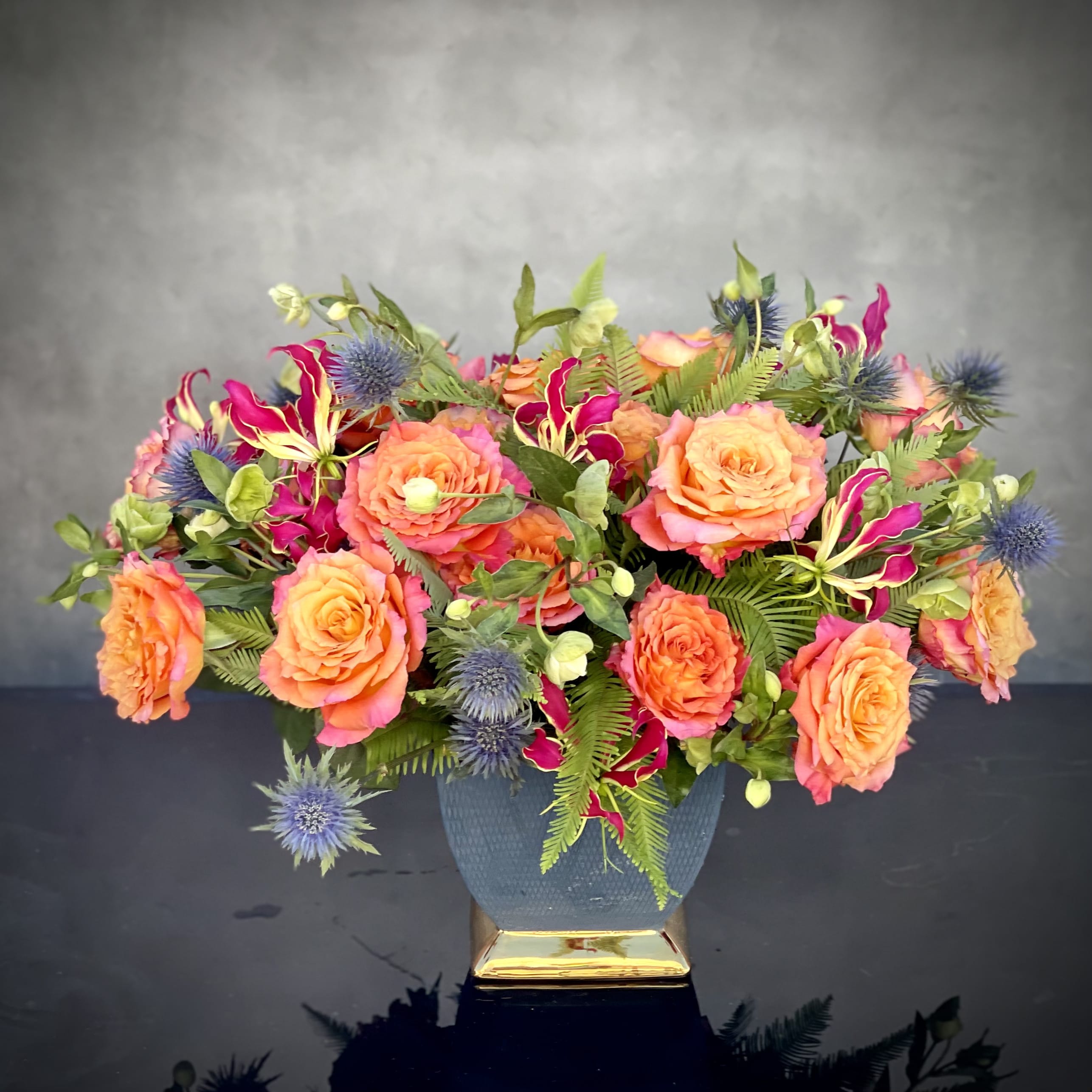 A Love Story - Amidst a cluster of beautiful multi-pigmented Roses of extraordinary hues are artfully placed to create this divine design.  Seasonal buds and greens and blue accent the blend of gorgeous blooms. This arrangement is ideal for any gift-giving occasion or to send sentiments of love or friendship.  