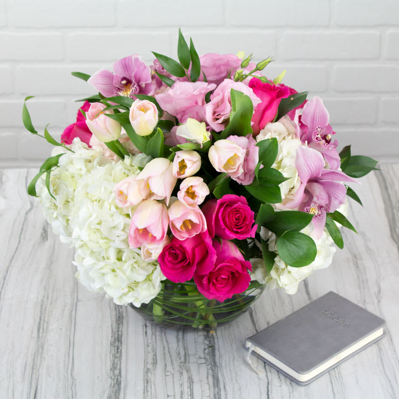 Pink and white mixed bouquet in a glass vase beside a small book