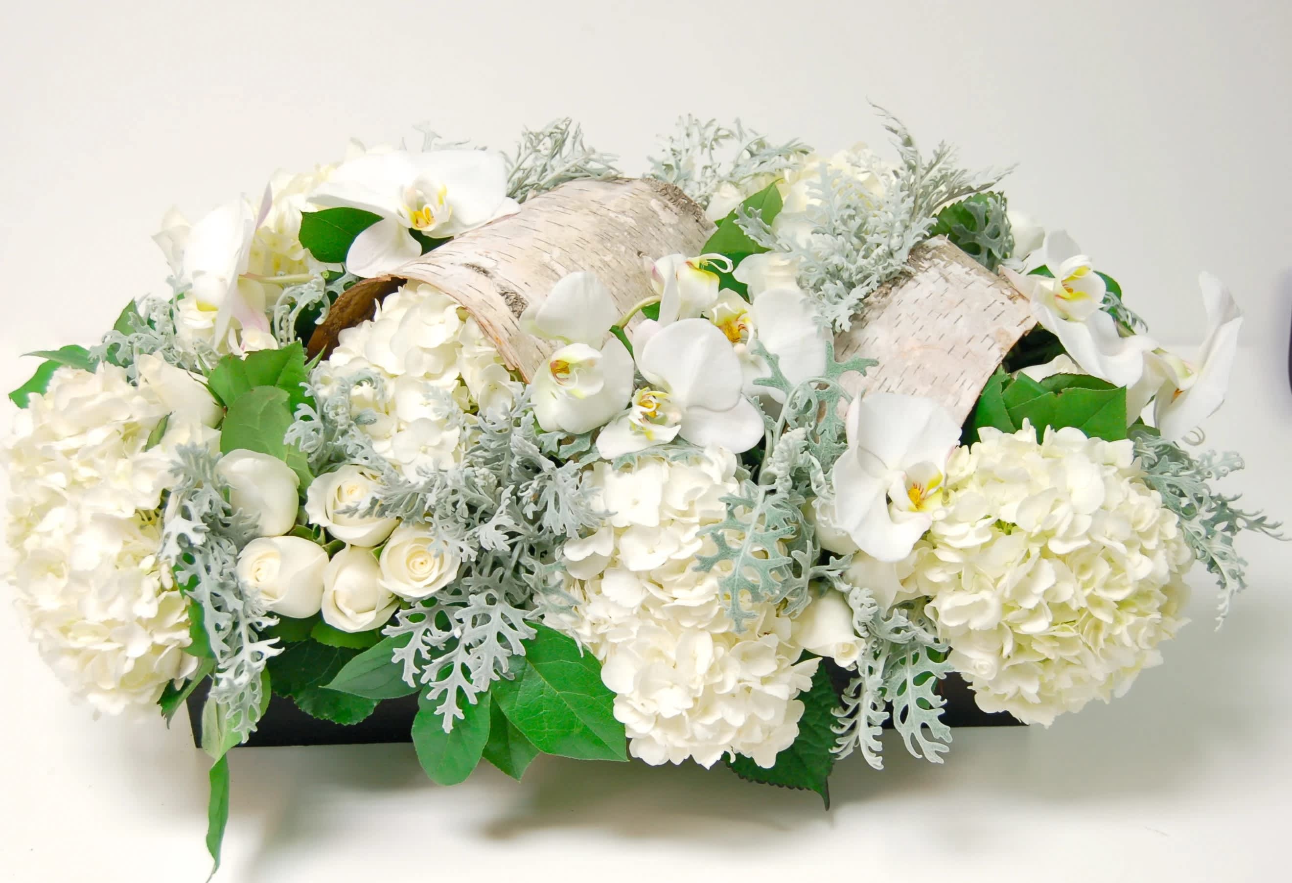 White floral arrangement with orchids and hydrangeas in a low container