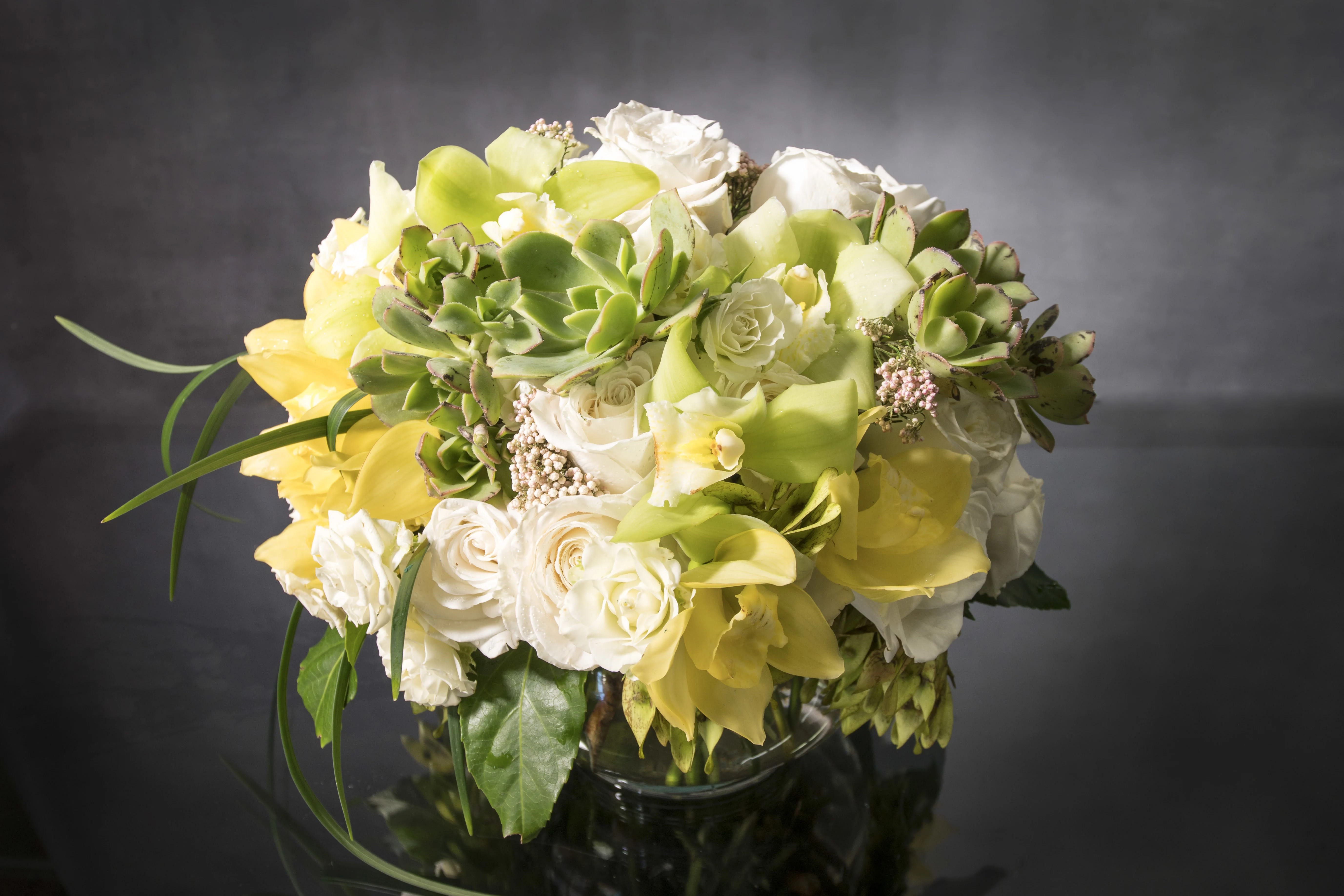 Bouquet of white roses and yellow calla lilies with succulents in a glass vase