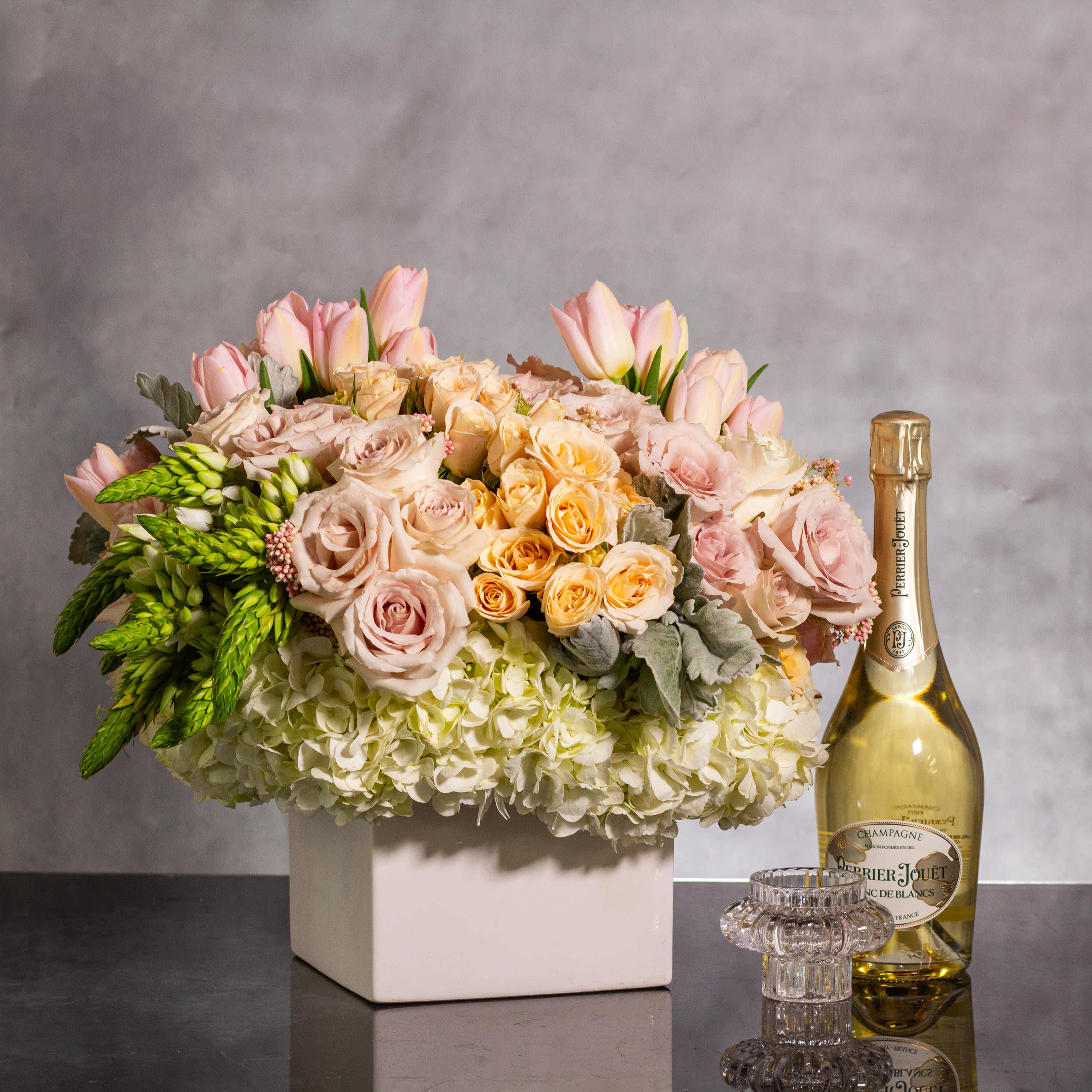 Pastel Garden Whispers -  Delight in the gentle beauty of our floral arrangement, featuring soft pastel hues and exquisite textures. This enchanting ensemble showcases a harmonious blend of garden roses, hydrangeas, and beautiful foliage, creating a lush and sophisticated display.  Nestled in a square white ceramic base measuring approximately 15 inches round, these compact flowers exude elegance and charm. The soft and dainty appearance of the blooms, paired with the intricate foliage, adds a touch of whimsical grace to the arrangement.  Perfect for adding a touch of serenity to any space, this pastel garden masterpiece is a celebration of delicate beauty and subtle sophistication. Elevate your surroundings with the ethereal charm of our Pastel Garden Whispers floral ensemble.