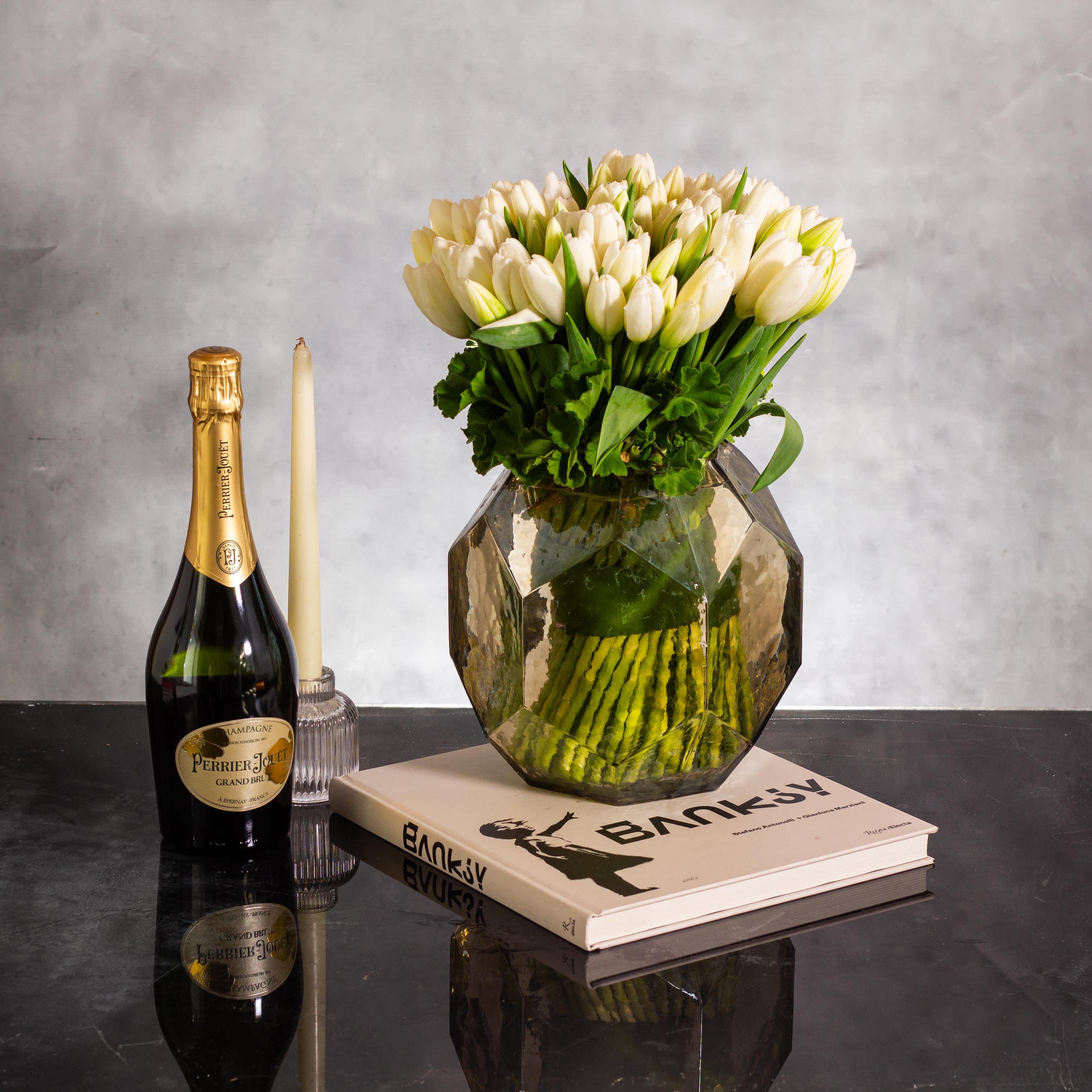 White Tulip Symphony - Indulge in a grand display of elegance with this stunning arrangement featuring 100 white tulips gracefully gathered in a beautiful water Hamburg-colored glass vase. The sheer abundance of delicate white tulips creates a sense of opulence and sophistication, making it a truly mesmerizing focal point.  Set in a Hamburg-colored glass vase, this arrangement not only showcases the purity and beauty of the white tulips but also adds a touch of modern allure with its unique vessel. The large number of tulips enhances the sense of luxury and grandeur, making it a breathtaking centerpiece that exudes timeless charm.  Perfect for making a statement at any event or as a lavish gift for someone special, this grand display of 100 white tulips in a Hamburg-colored glass vase is a true celebration of beauty and refinement.