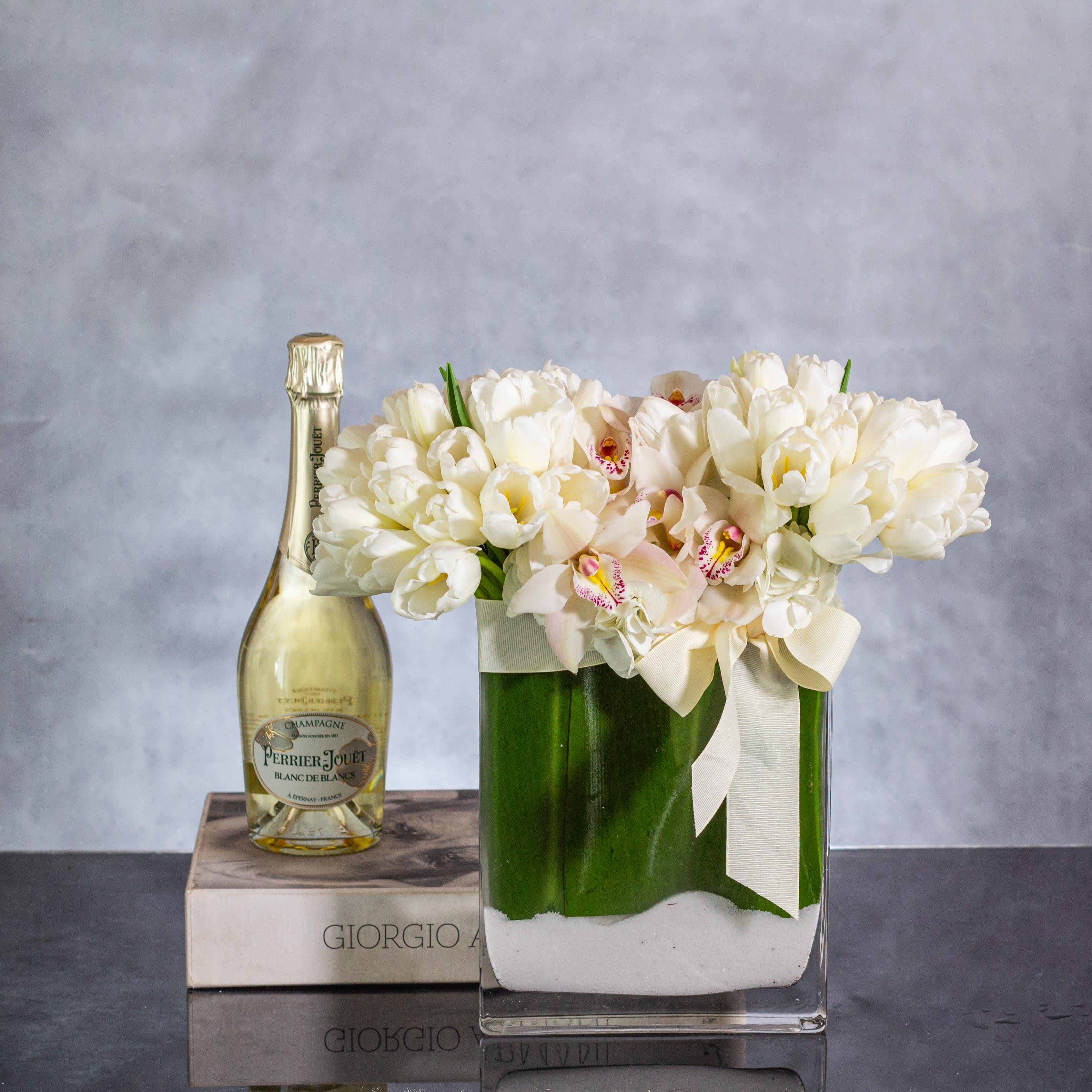 Serene Elegance - Delight in the serene beauty of this exquisite floral arrangement featuring a lavish grouping of 50 pristine white tulips and delicate white orchids artfully displayed in a rectangular base adorned with lush green leaves and sand accents. The pure elegance of the white blooms, combined with the natural elements, creates a harmonious blend of sophistication and tranquility.  For those in Beverly Hills and surrounding areas seeking a touch of luxury and refinement, this arrangement offers a timeless charm that is both graceful and enchanting. With same-day delivery available, surprise your loved ones or elevate your own space with this stunning display of white tulips and orchids that exudes serenity and beauty.