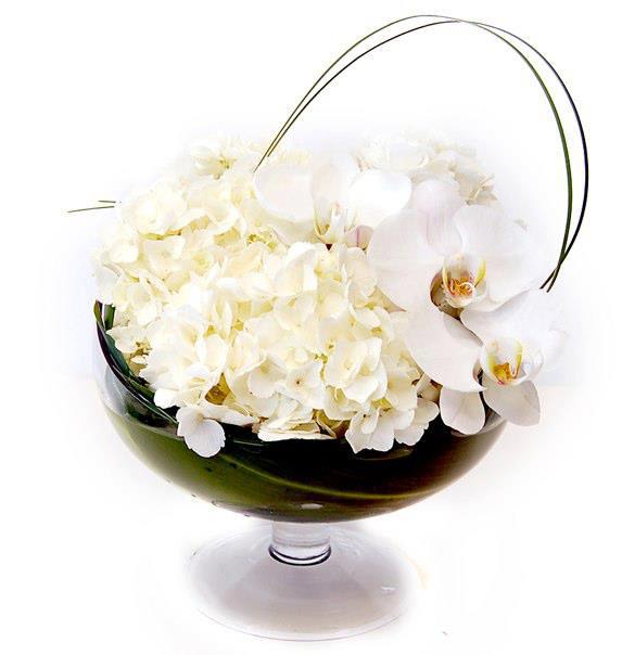 Low arrangement of white hydrangeas and orchids in a clear glass pedestal bowl