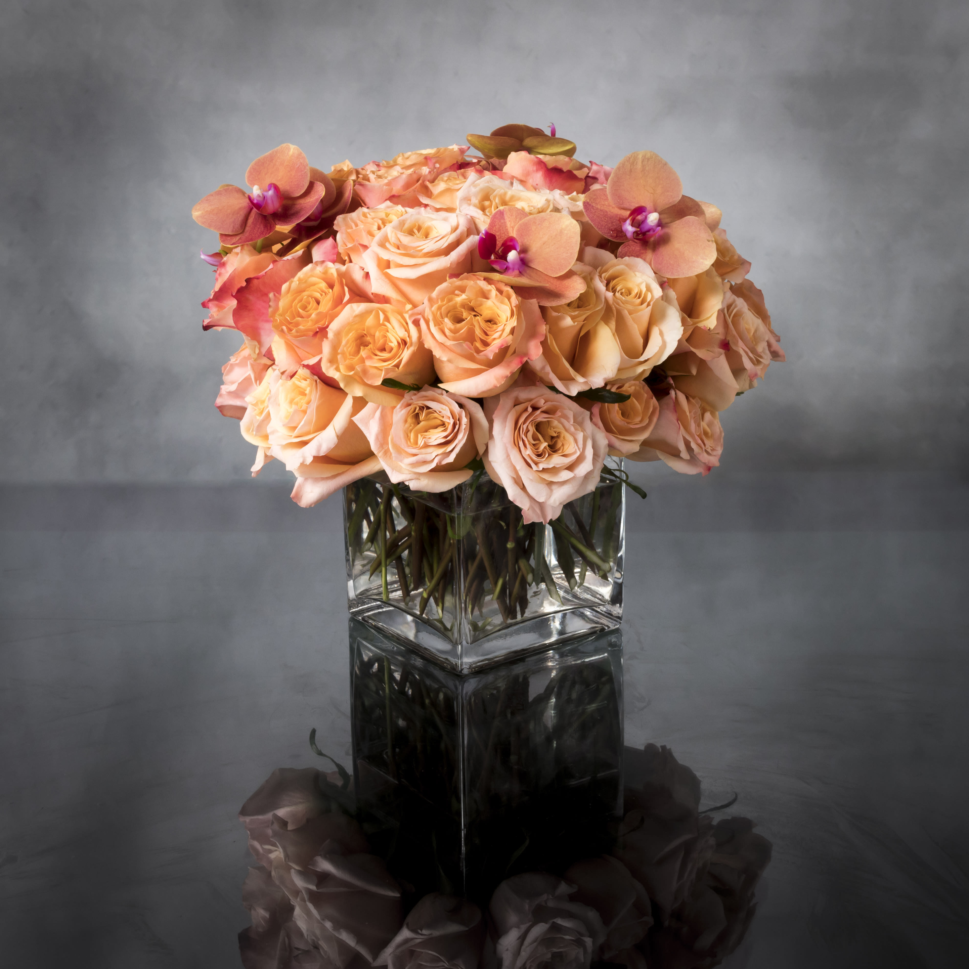 Cherry Brandy Charm - Pasadena Florist - Bold and dynamic, this stunning display of Cherry Brandy roses and garden roses with orchids will drop the jaw of any onlooker. Beautifully presented in glass vase, these gorgeous roses will say what's in your heart more eloquently than words.  Standard: 2 Dozen Roses  Deluxe: 3 Dozen Roses  Premium: 4 Dozen Roses  Deluxe as shown