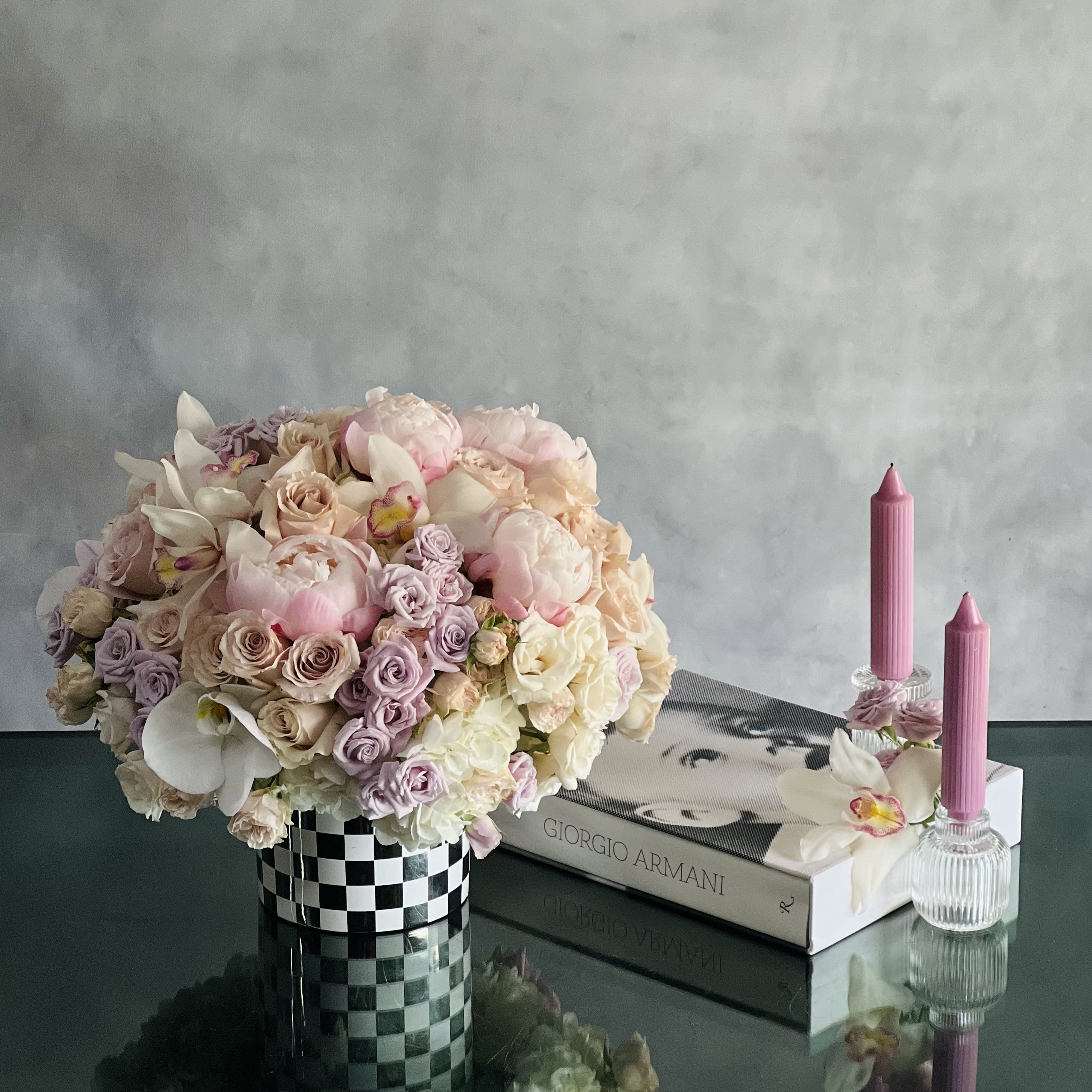 Checkmate - Pasadena Florist - This beautiful array of light pink peonies, pink roses, lavender and light pink spray roses, white orchids nested on white hydrangeas in a beautiful checked ceramic vase will melt your heart away. 