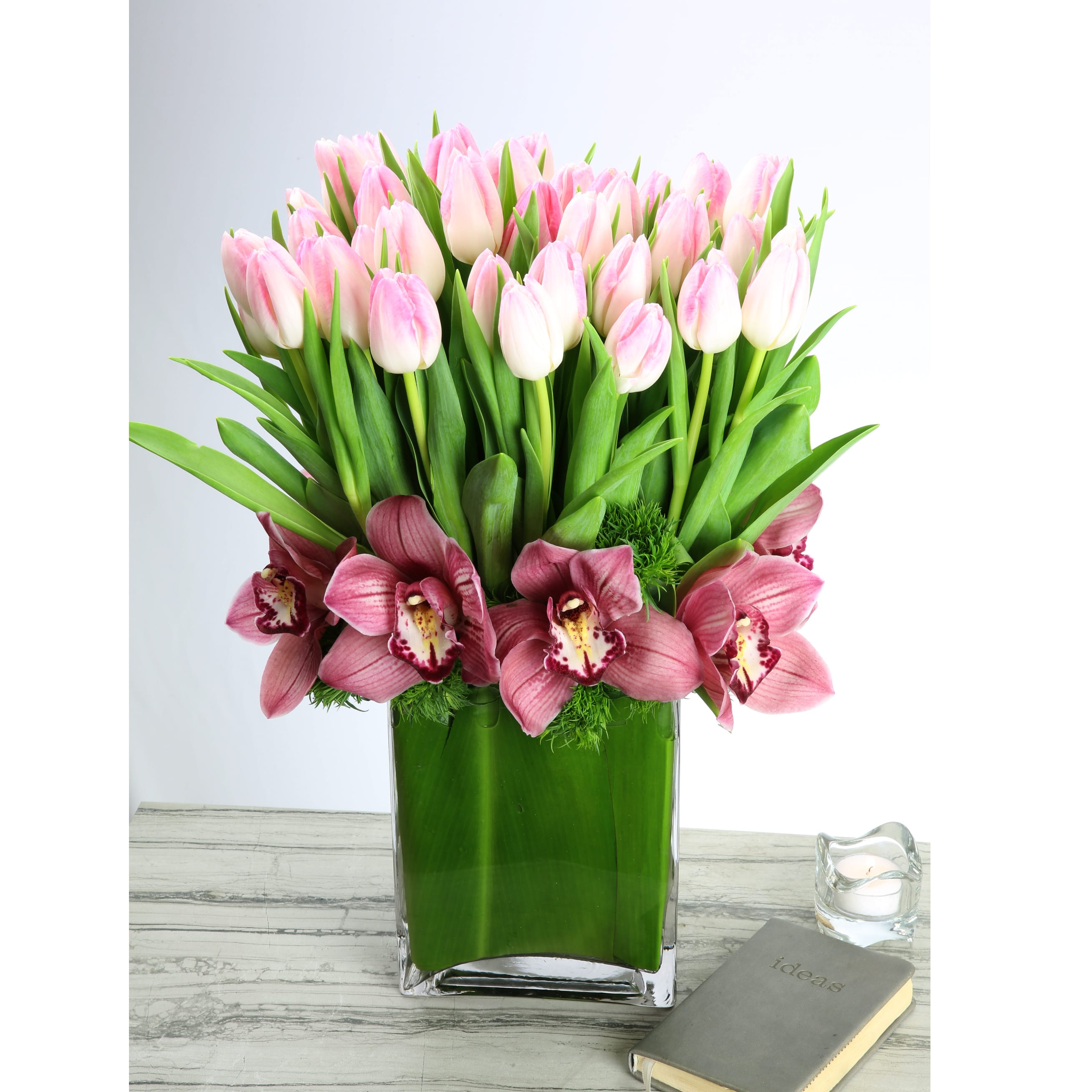 Blissfully Beautiful  - Share the ultimate serenity of 50 pristine light pink Dutch Tulips standing tall in this leaf-lined glass vase, while stunning white Orchids dance at the base. This beautiful design will accent any décor with its elegance and classically timeless beauty.   Deluxe: 75 light pink Dutch Tulips and Orchids in a Glass Vase  Premium: 100 light pink Dutch Tulips and Orchids in a Glass Vase 