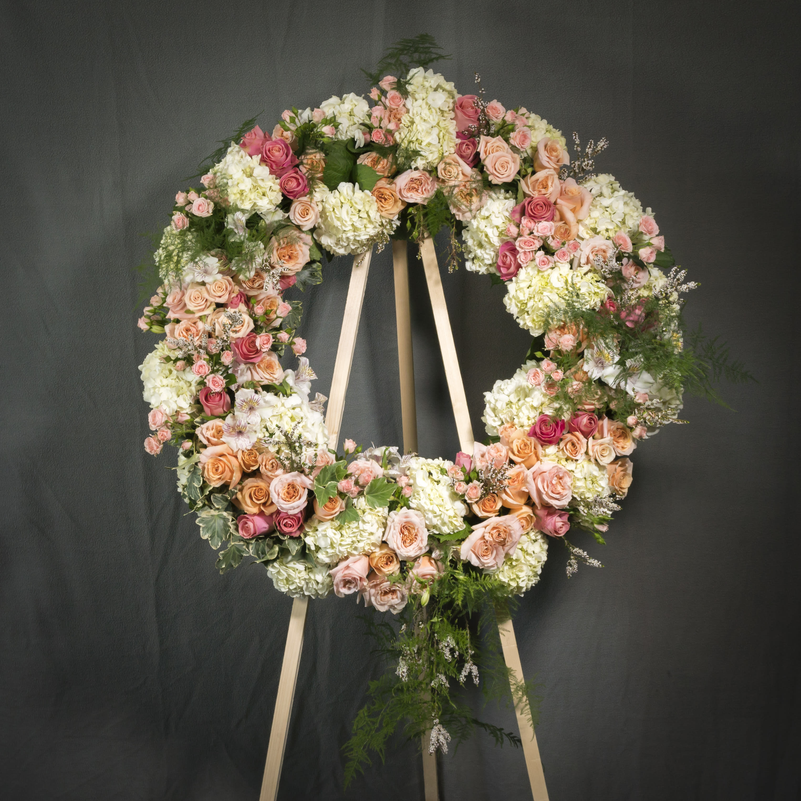 Large standing wreath of peach and pink roses with white hydrangeas on a wooden easel