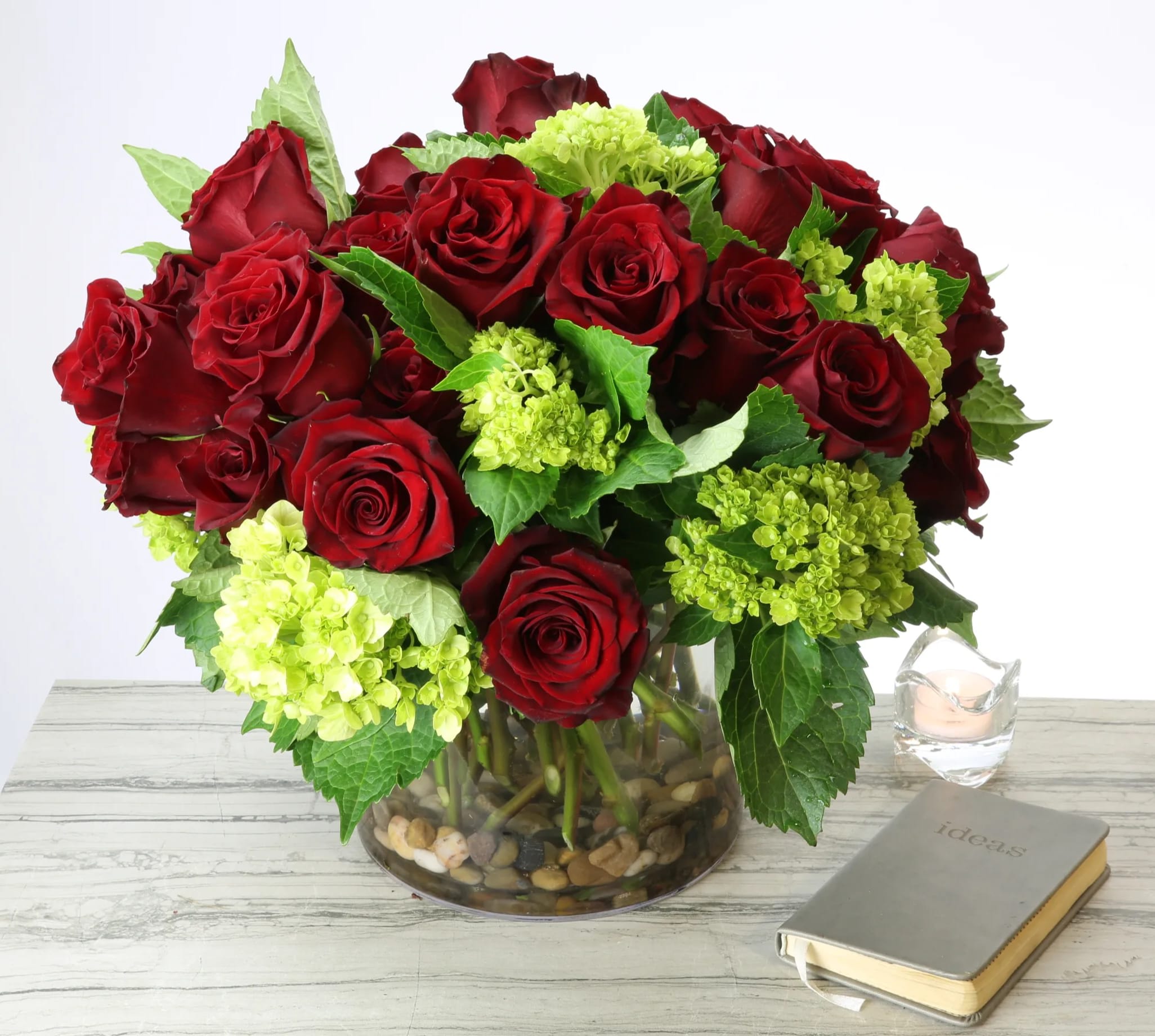 Sweet and Sour - This lovely arrangement features 2 Dozen vibrant Ecuadorian red Roses clustered in a round bouquet contrasted with scattered mini bunches of lime Hydrangeas and seasonal greens. A stunning arrangement that can be a great winter holiday gift or table centerpiece. 6X6" glass vase. 12" round.   Deluxe: 3 dozen roses  Premium: 4 dozen roses