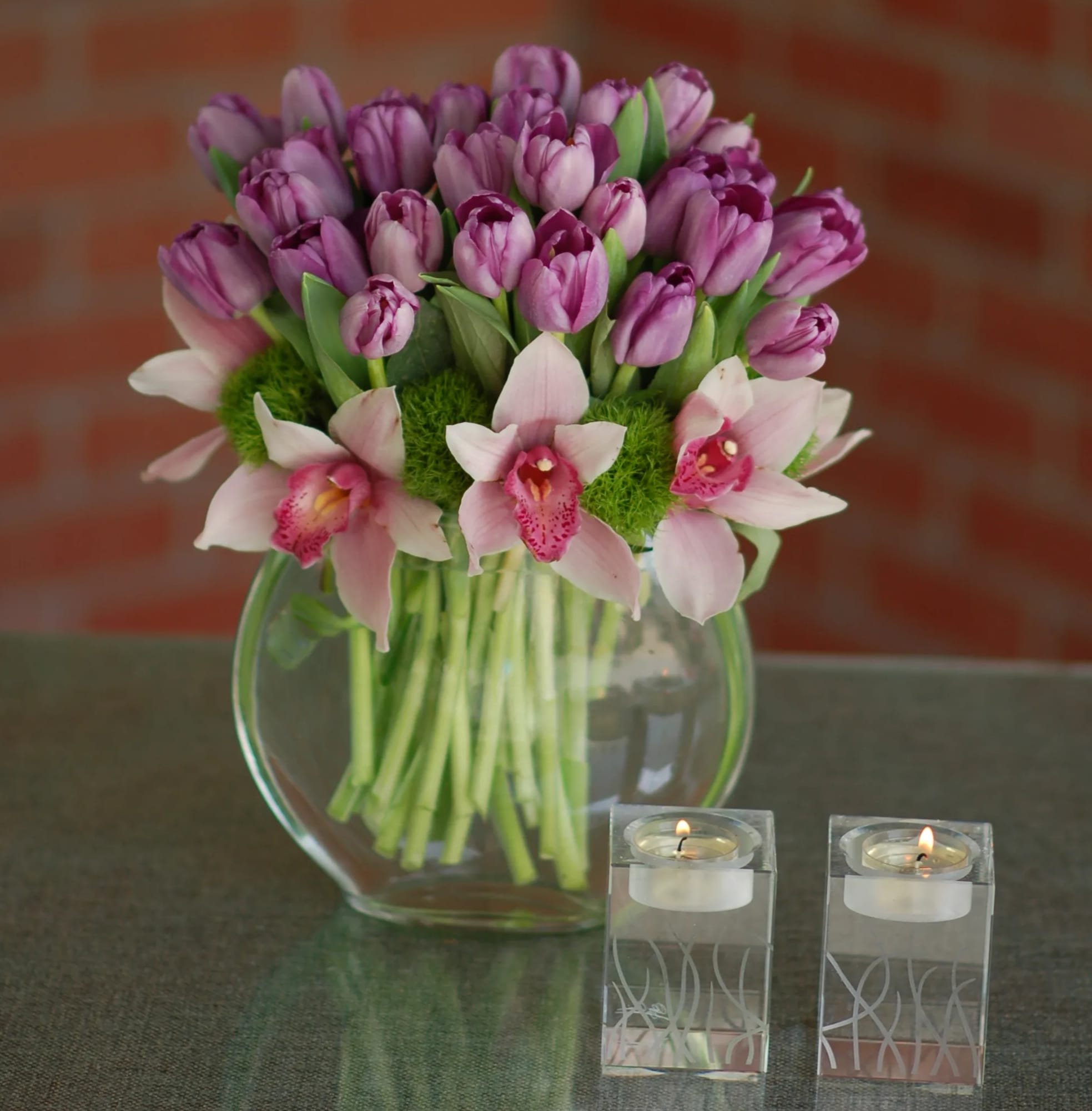 Pretty Little Thing  - My Sherman Oaks Florist presents a beautiful array of Purple Tulips that are accented with White Cymbidium Orchids. Which are then placed together in a clear circular glass vase. This piece fits perfectly in a home or office and adds brightness to the room. 