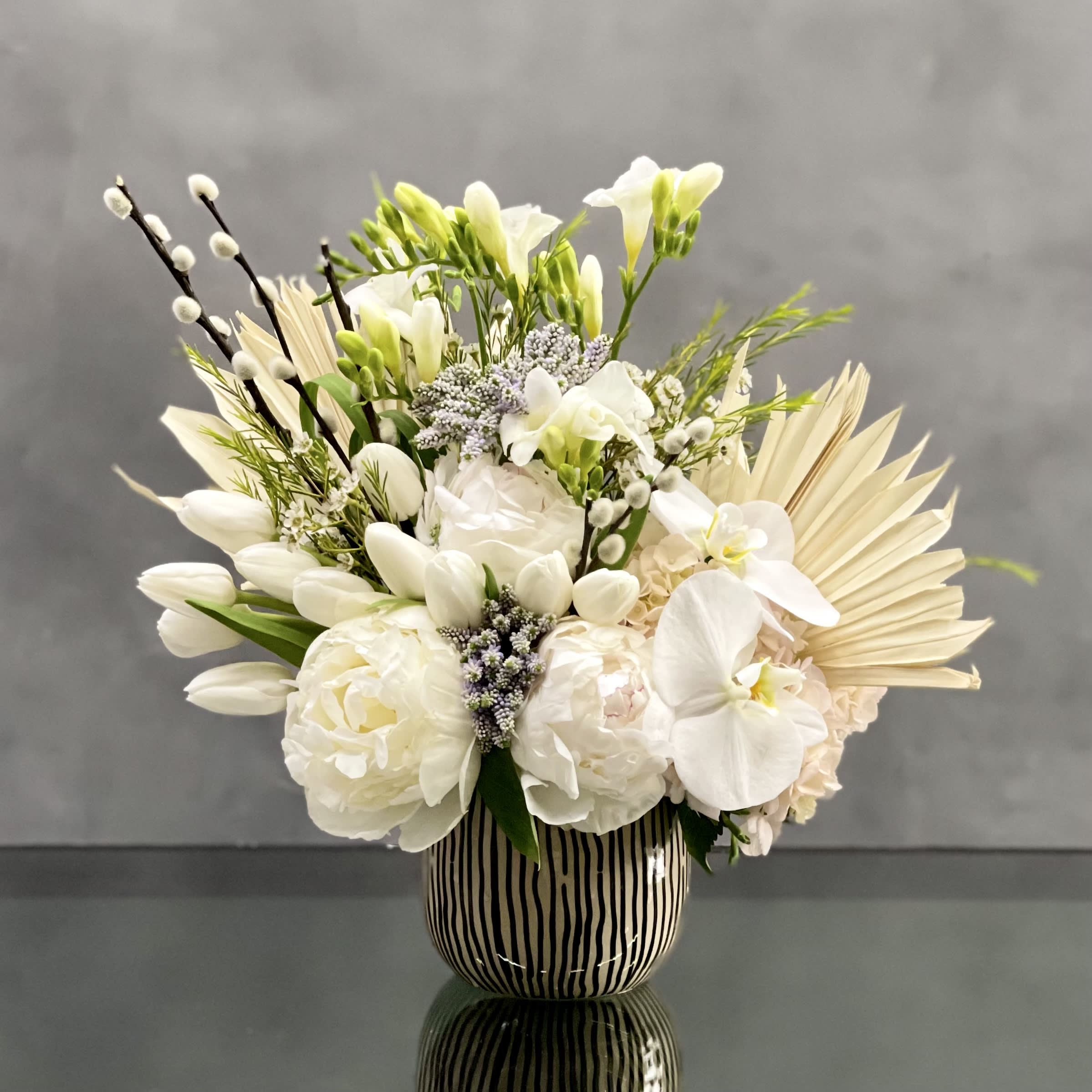 Designer's Choice - White - This arrangement is made with a designer's choice array of seasonal white flowers. Floral could include Roses, Hydrangeas, Orchids, Tulips and or Peonies. These beautiful white flowers are an excellent choice for weddings, funerals and other major life events.   
