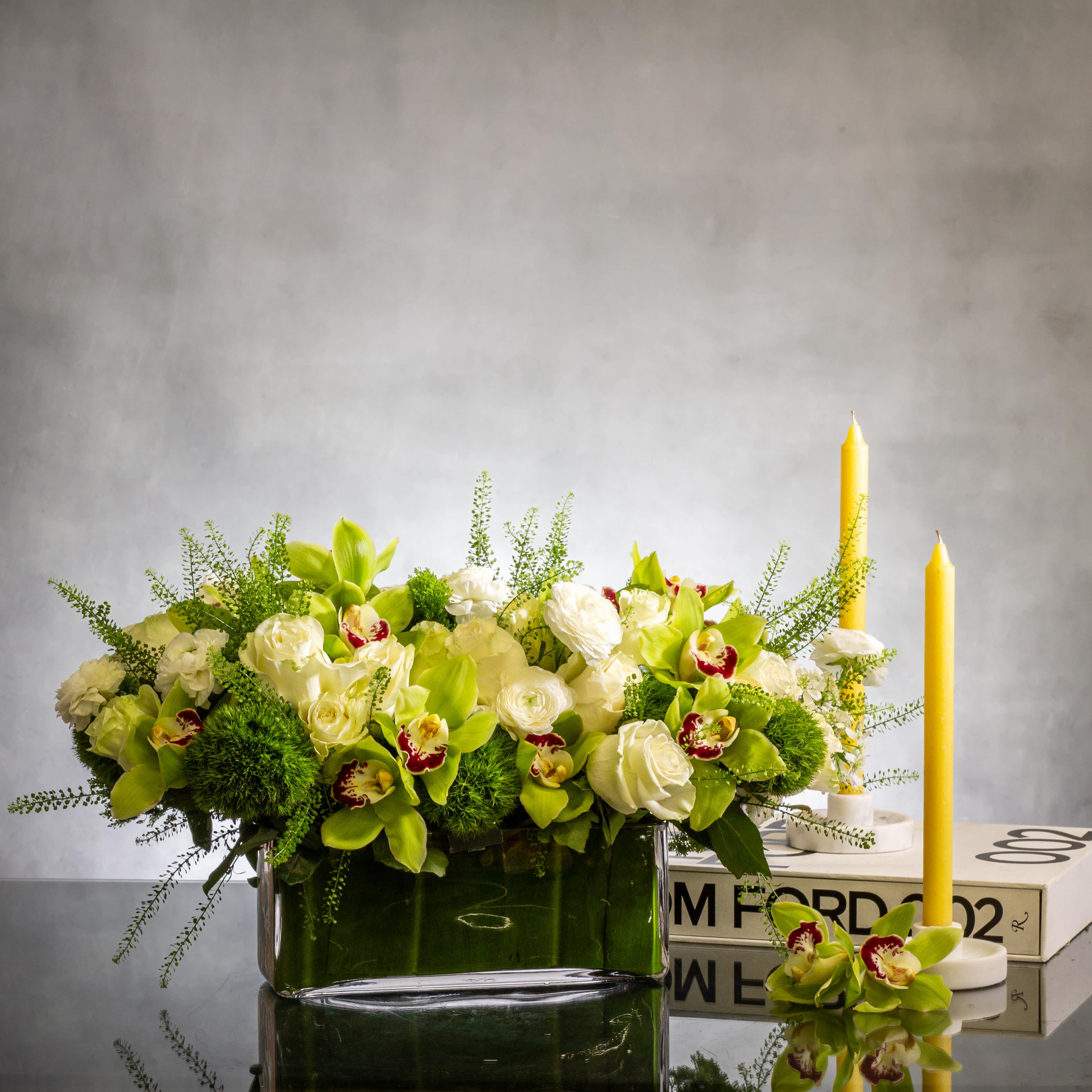 Green and White Classic - Indulge in the captivating beauty of nature with our exquisite floral arrangement featuring vibrant green orchids and timeless classic white roses. Carefully arranged in a sleek and modern 9" x 4" rectangular glass vase,&nbsp;arrangement approx. 16" and 8" Tall long.&nbsp; &nbsp; this stunning composition effortlessly blends elegance with contemporary style. The striking contrast between the lush green orchids and the pristine white roses creates a captivating visual display that is sure to leave a lasting impression. Whether as a heartfelt gesture or a stylish accent for your home or office, this arrangement is perfect for any occasion. Experience the beauty of nature brought to life with our green orchids and classic white roses arrangement..  Deluxe - 16" X 4" arrangement approx. 22" long and 9" Tall .