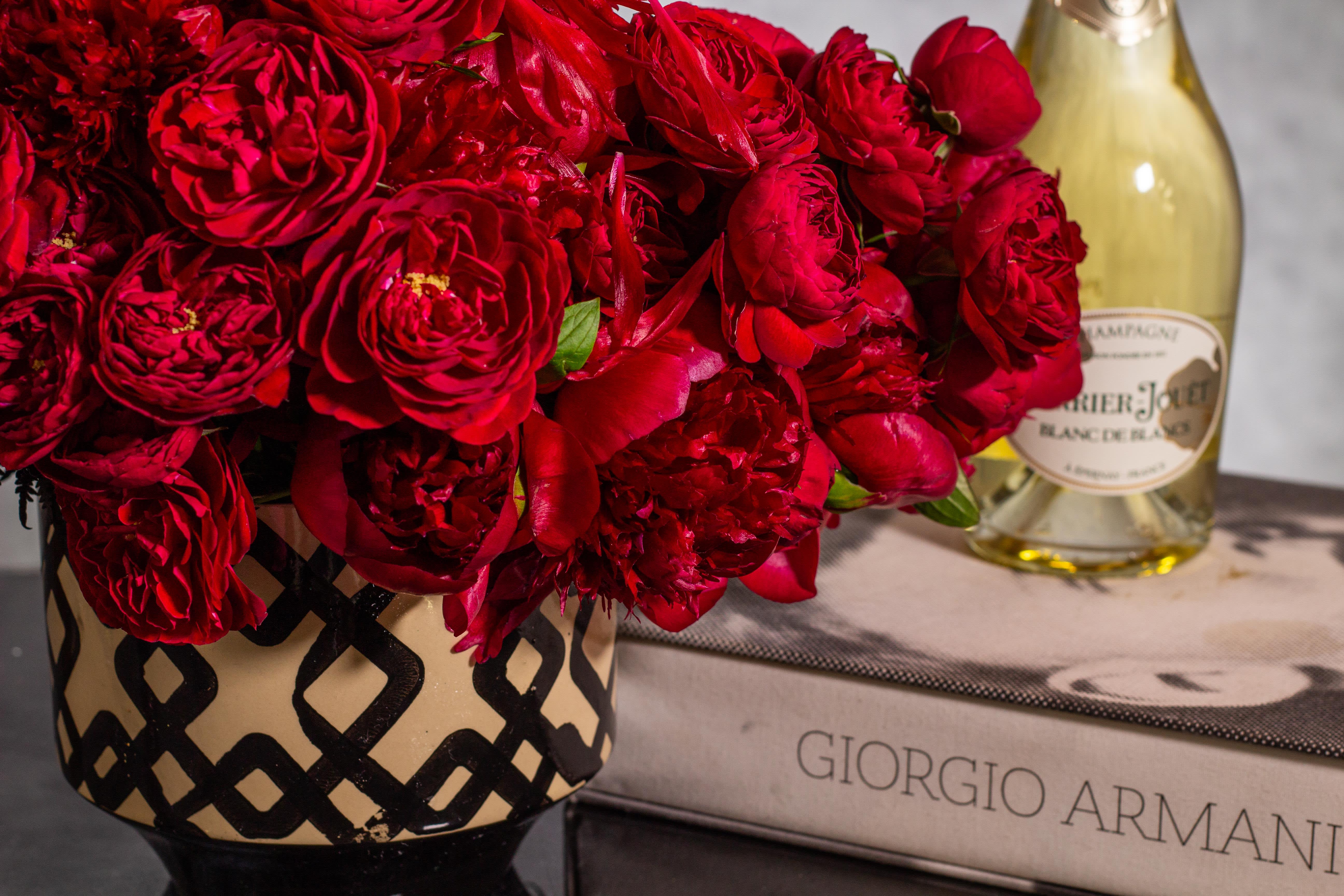 Red rose bouquet in a patterned vase beside a champagne bottle and gift box