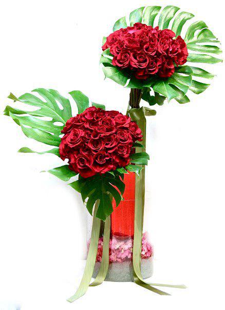Tall modern arrangement of red roses in two spheres with large tropical leaves in a glass vase