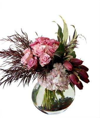 Pink roses, hydrangeas, and dark tulips arranged in a round glass vase.