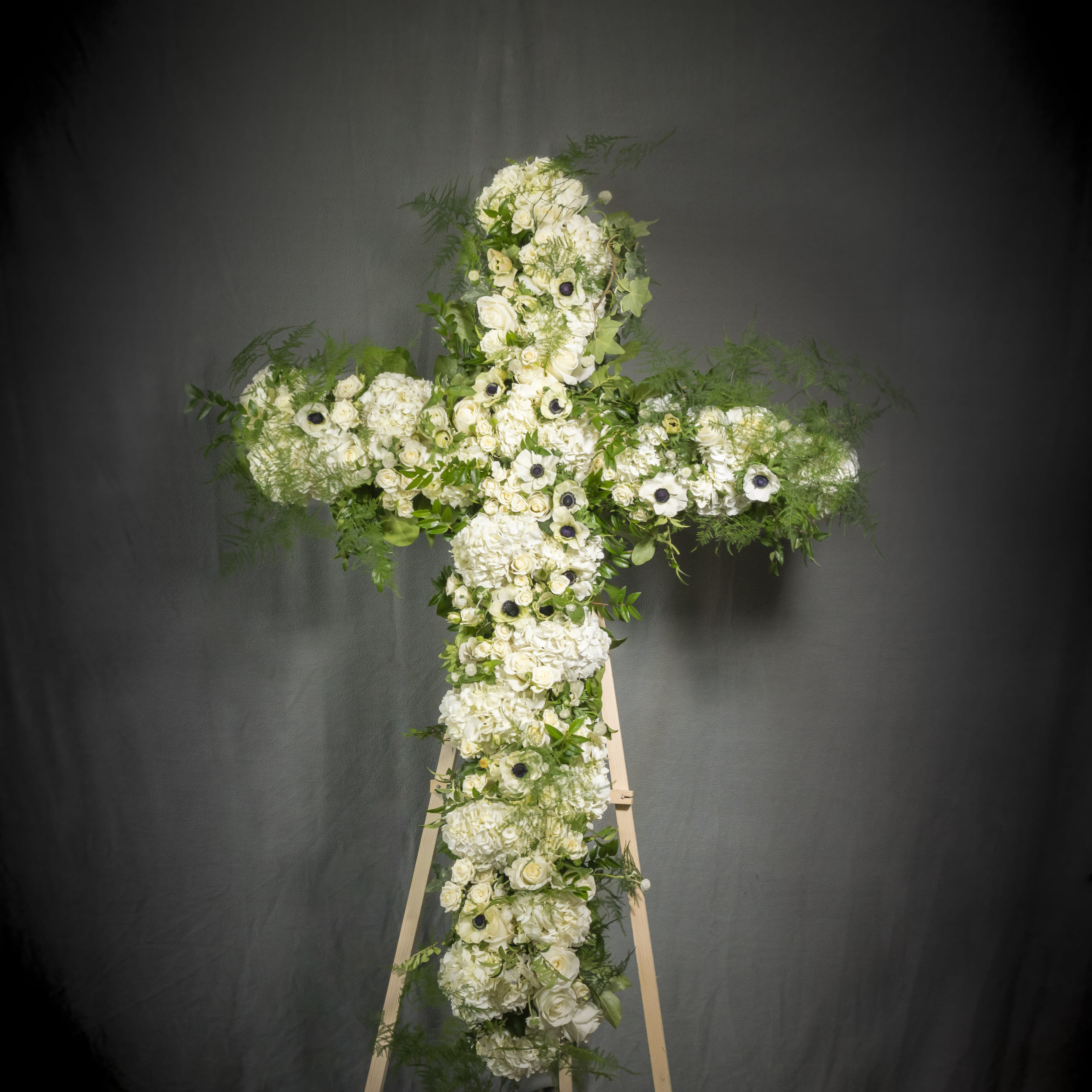 White Cross Wreath - A large white funeral wreath on a stand decorated in seasonal white blooms. An overflowing of love and respect is expressed in this truly magnificent standing spray.